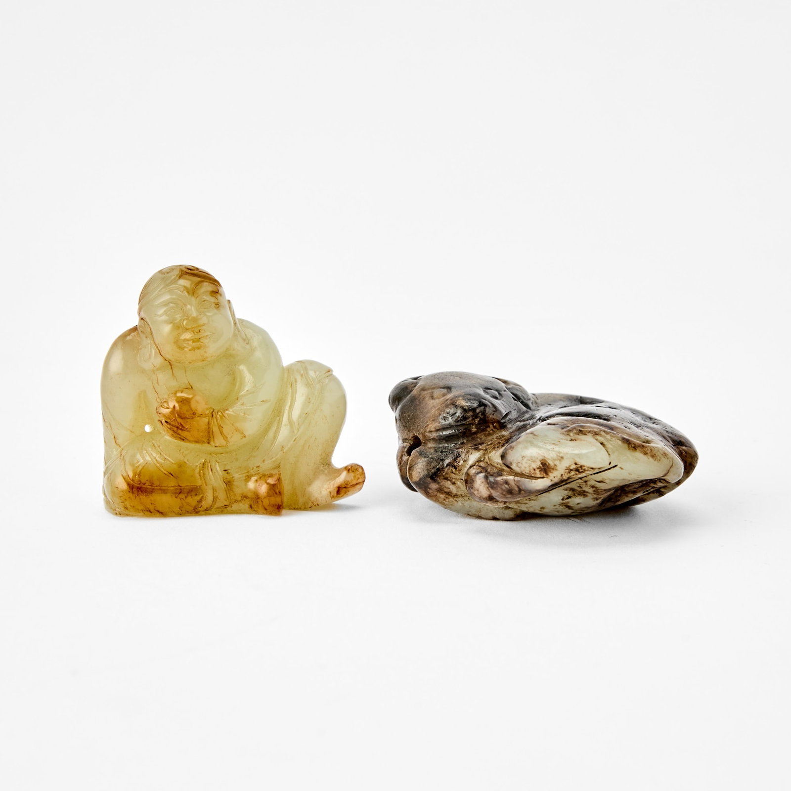 Two Chinese Jade Figural Carvings Early Qing Dynasty: One carved as Liu Hai half-reclining and holding a toad, the other carved as a recumbent water buffalo. (Length of largest 2 1/4 inches)