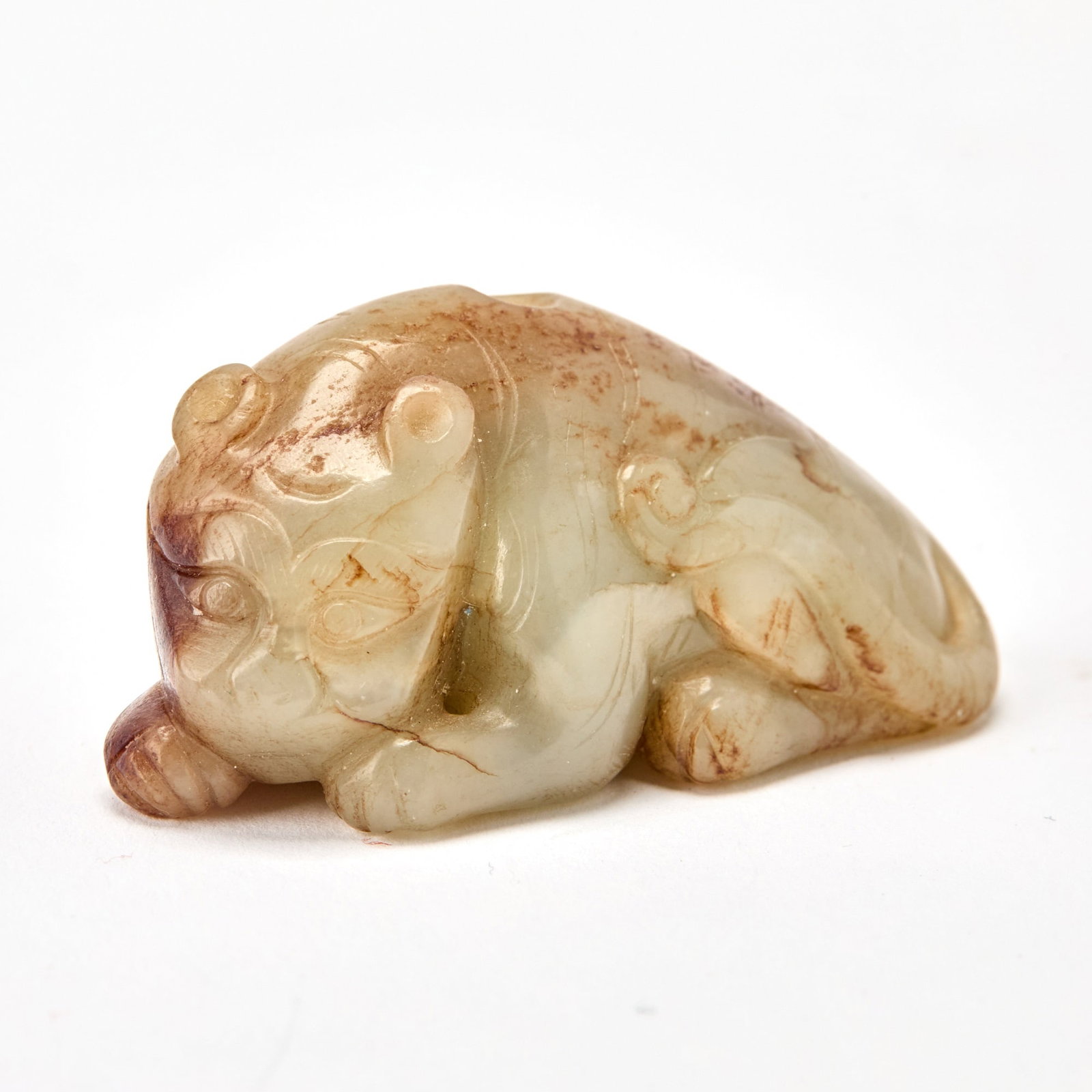 A Chinese Celadon Jade Toggle of a Tiger Song Dynasty: Carved in a recumbent position, with its tail flicked upward; the sonte of brown and russet coloring and inclusions. (Length 2 inches)