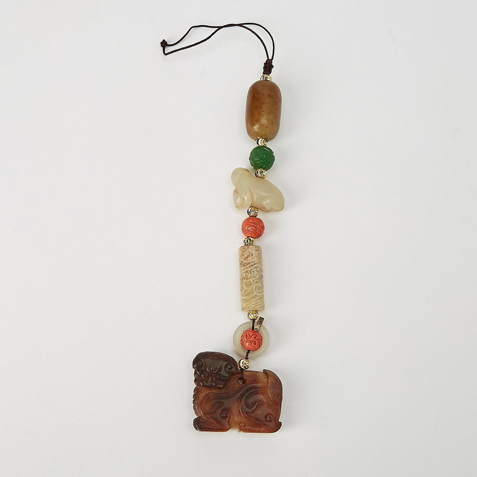 A Chinese String of Jade and Coral Pendants Qing Dynasty and Earlier: Comprising a string of coral beads and carved jade ornaments, including pieces in the form of mythical beasts and archaistic motifs. (Length 7 inches)