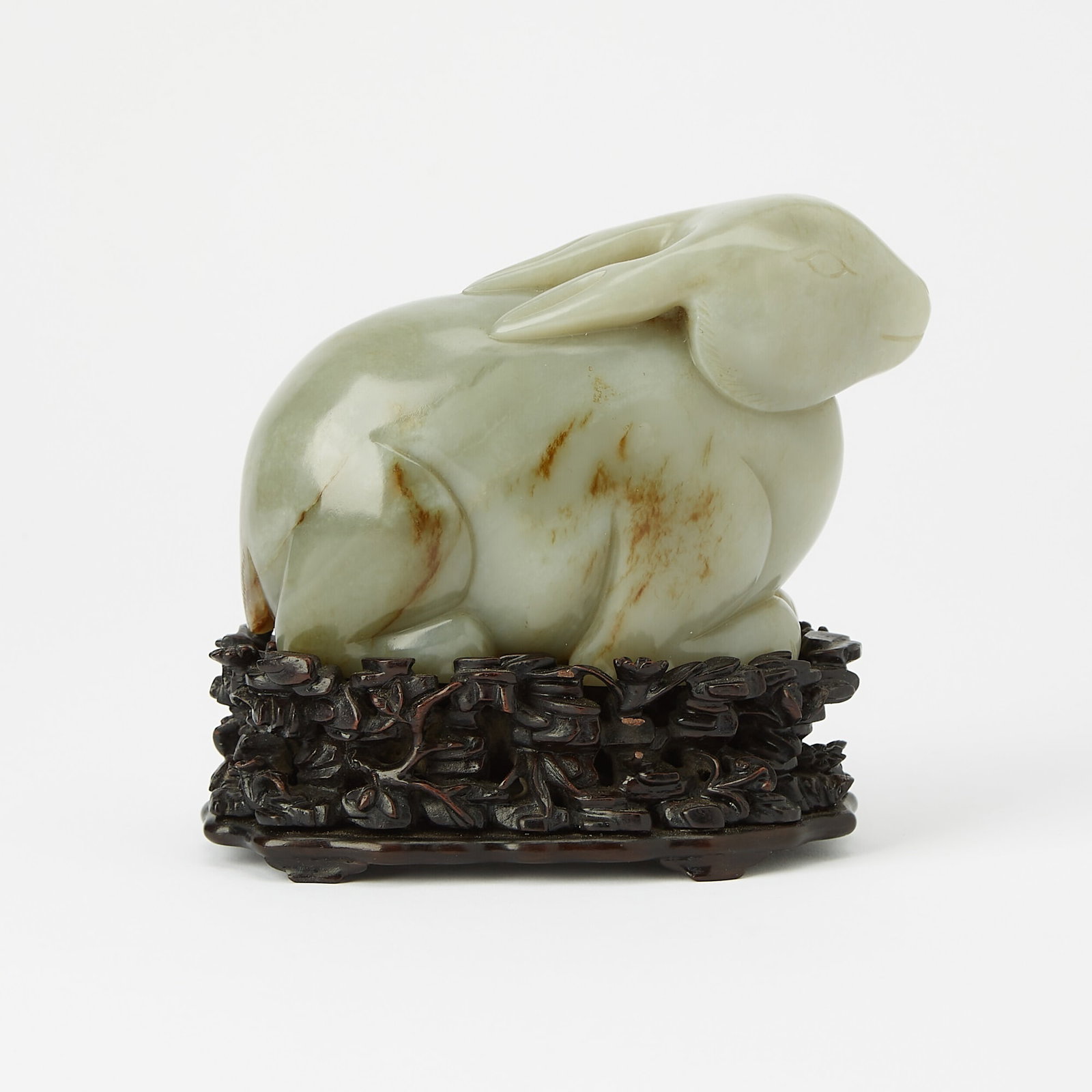 A Chinese Greyish Celadon Jade Rabbit Qing Dynasty: Carved in a recumbent position, with legs tucked under the body and ears laid back; with a fitted hardwood stand. (Length 5 1/4 inches)