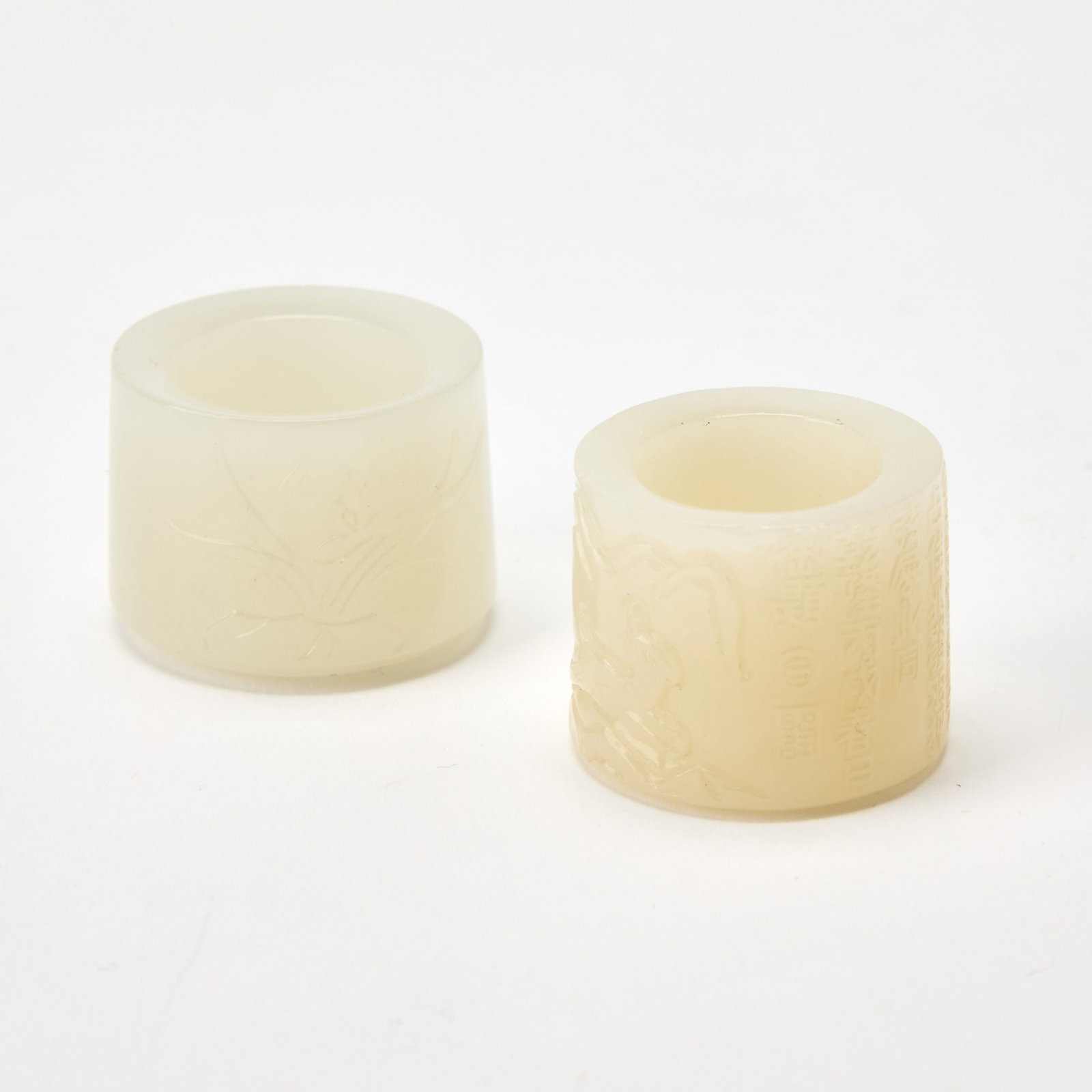 Two Chinese Carved White Jade Thumb Rings One with Qianlong Mark, 18th Century: Comprising an example carved with an orchid flower, and the other one carved with an equestrian hunting a deer. (Diameter of largest 1 1/4 inches)