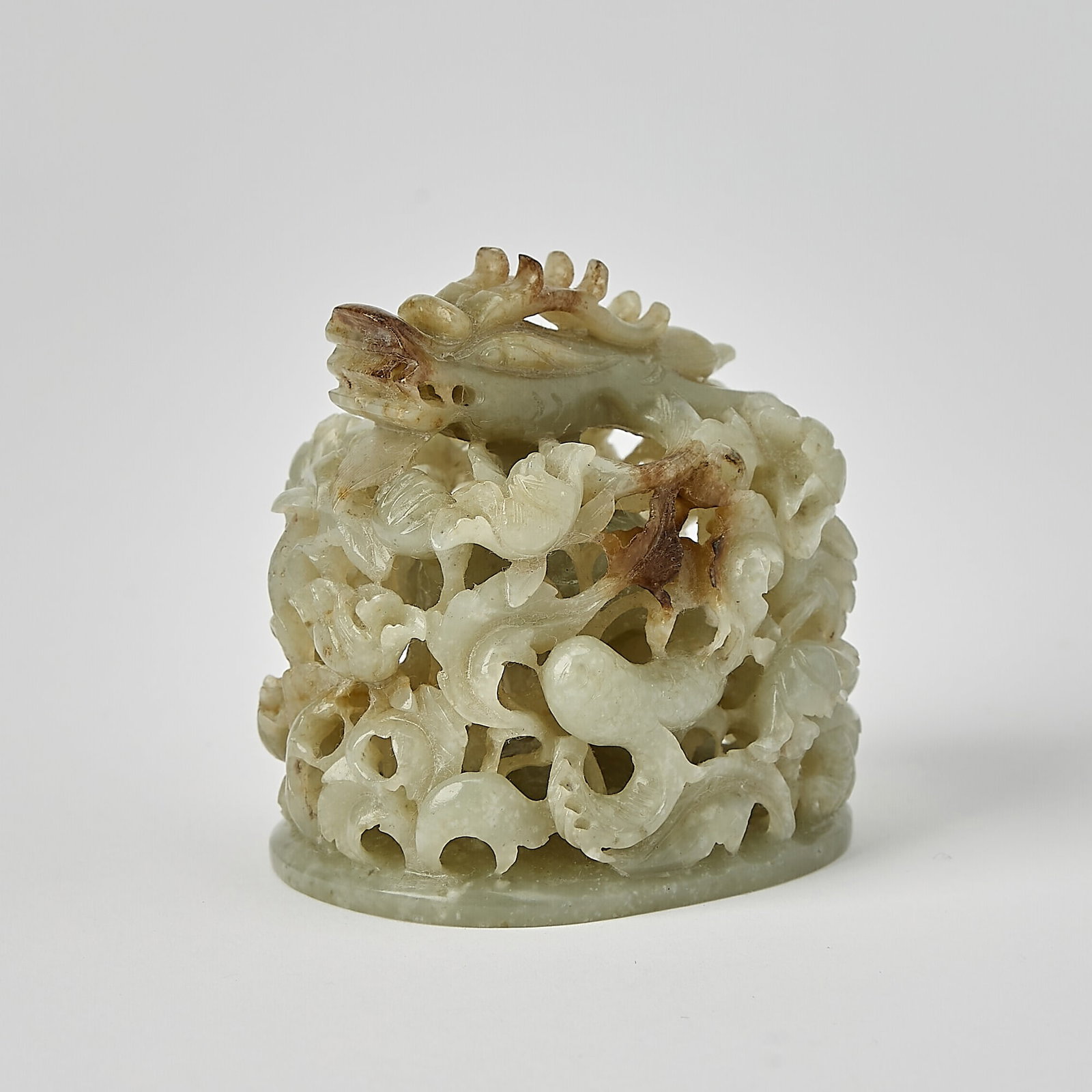 A Chinese Celadon Jade Finial Ming-Qing Dynasty: Carved in openwork with a coiling dragon emerging from dense, intricately carved blossoming and leafy vines. (Height 3 inches)