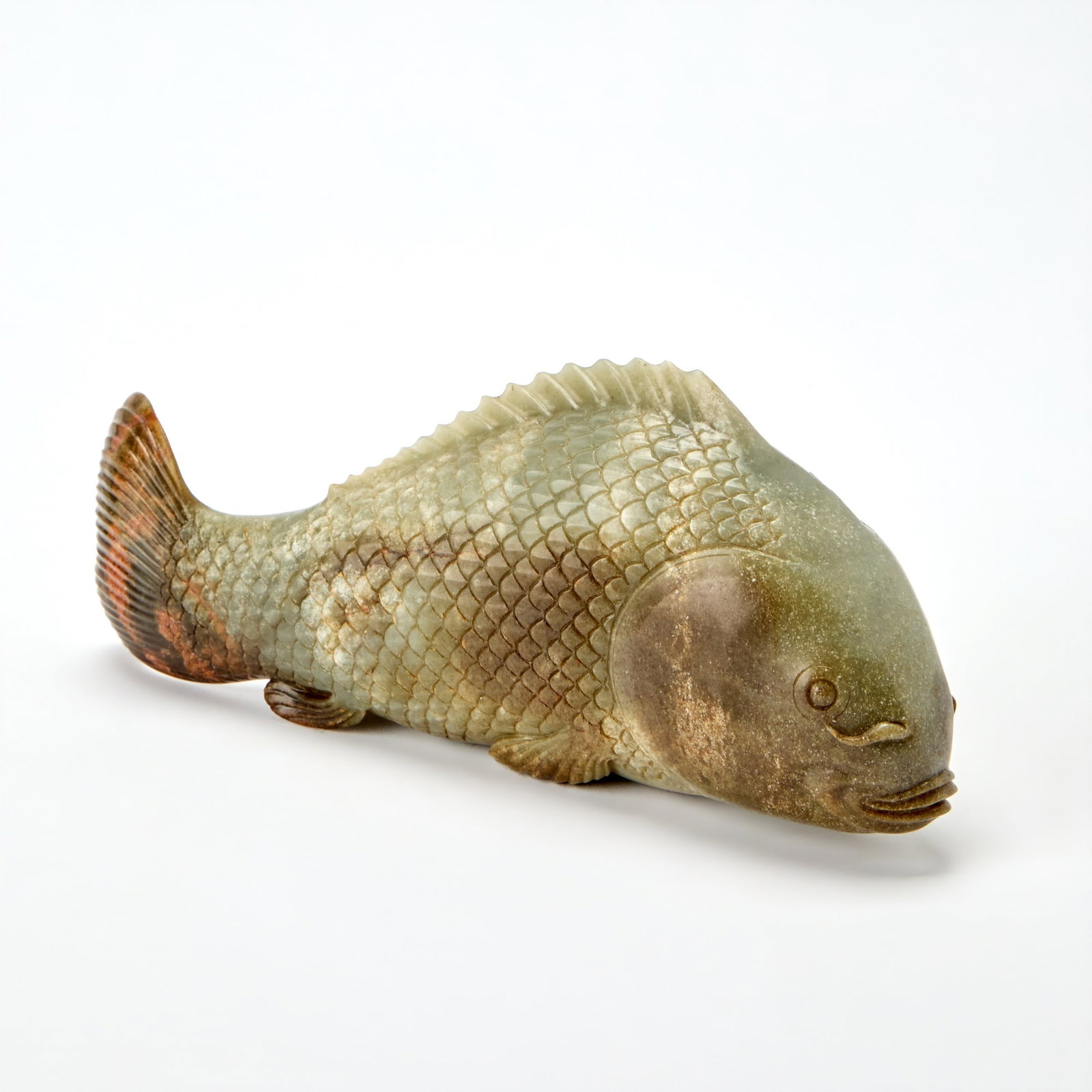 A Chinese Celadon Jade Carp Probably Late Qing Dynasty: The body carved with overlapping scales, the stone of mottled tones with russet and brown inclusions. (Length 10 inches)