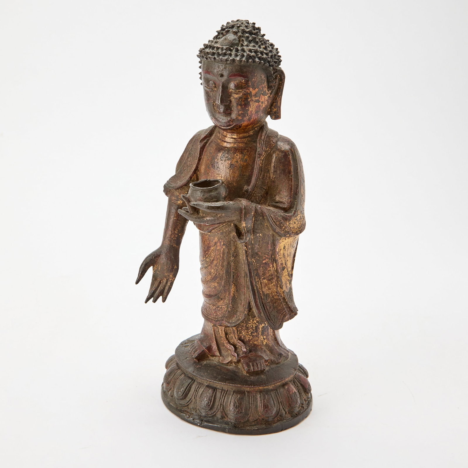 A Chinese Gilt Lacquered Bronze Figure of Shakyamuni Ming Dynasty: The figure standing on a single-lotus base, dressed in long, flowing robe engraved with decorative scrolls, holding an alms bowl in his left hand. (Height 12 1/2 inches)