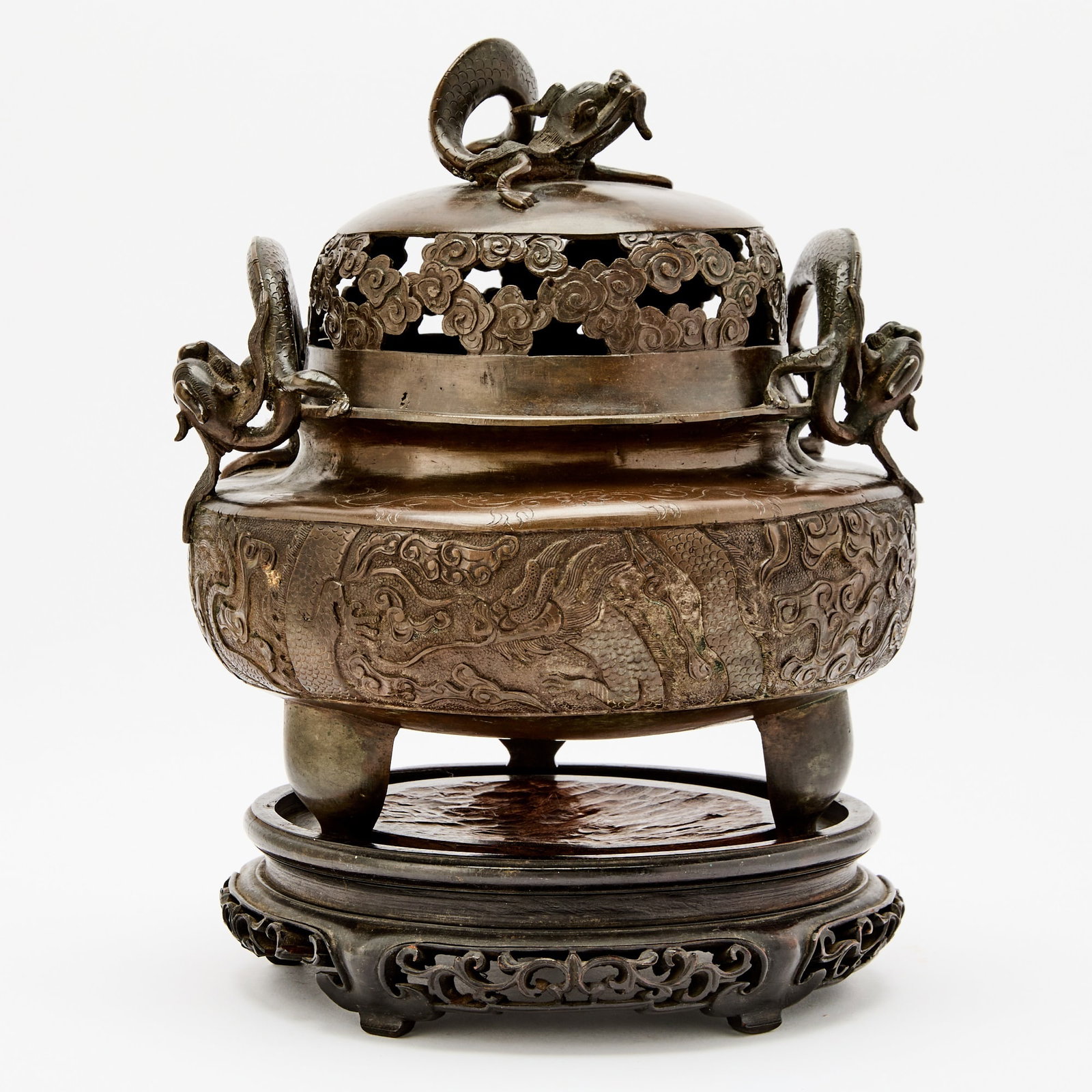 A Chinese Cast Bronze Censer and Cover Qing Dynasty: Of compressed form, supported by three splayed legs, and surmounted by a reticulated cover, the exterior decorated with panels featuring dragons and cloud scrolls; the underside impressed with a mark 