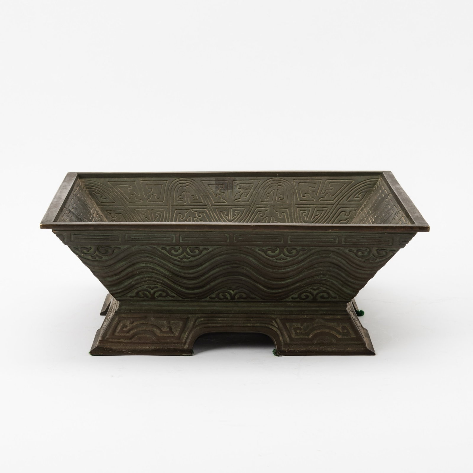 A Chinese Cast Bronze Square Censer Qing Dynasty: Decorated with undulating wave bands and archaistic motifs, the interior adorned with a central floral design encircled by a stylized lappet band. (Length 11 3/4 inches)
