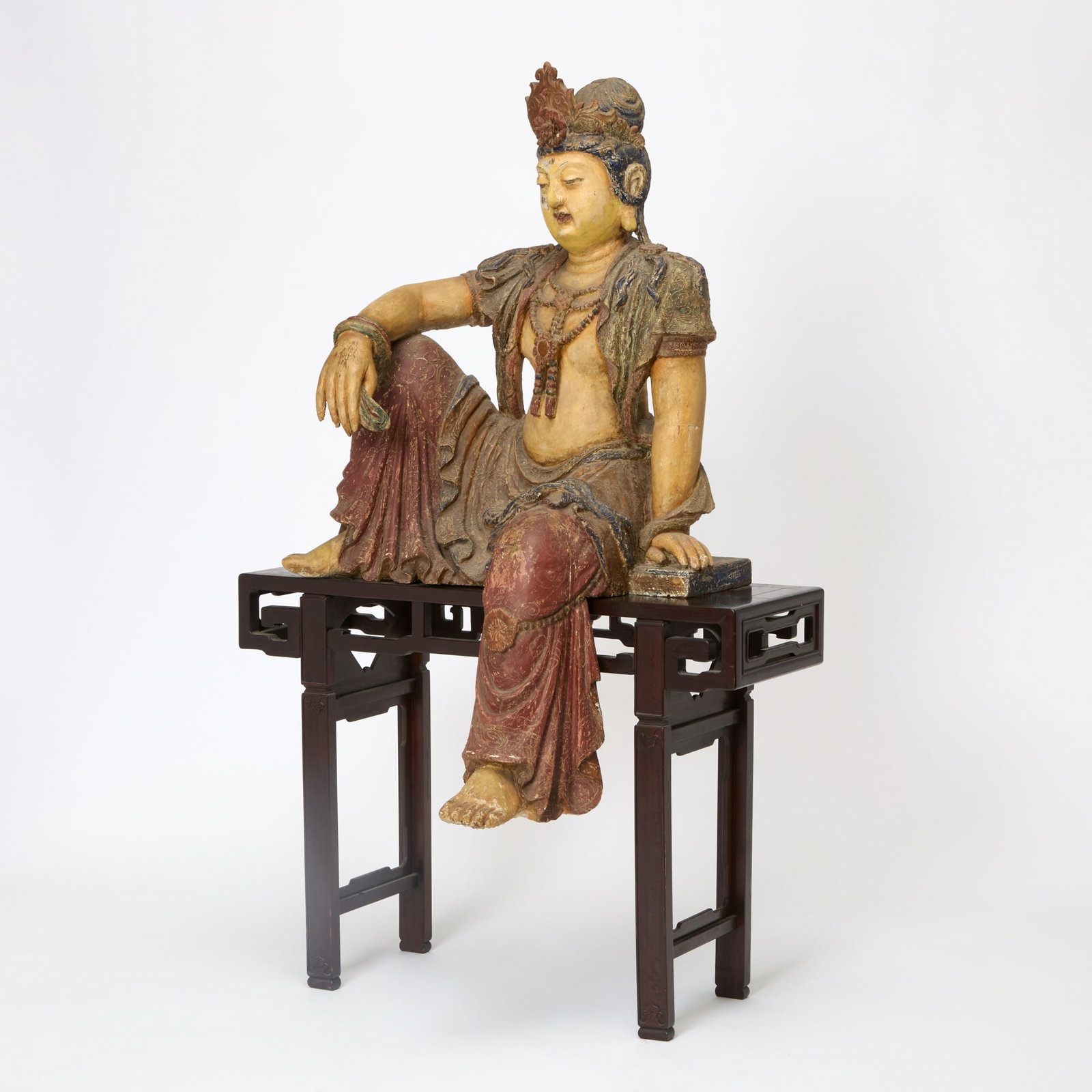 A Chinese Polychromed Wood Figure of Guanyin Ming-Qing Dynasty: Of typical depiction and carved and in the 'Water Moon' form with one leg raised; together with hardwood side table functioning as stand. (Height approximately 55 inches)