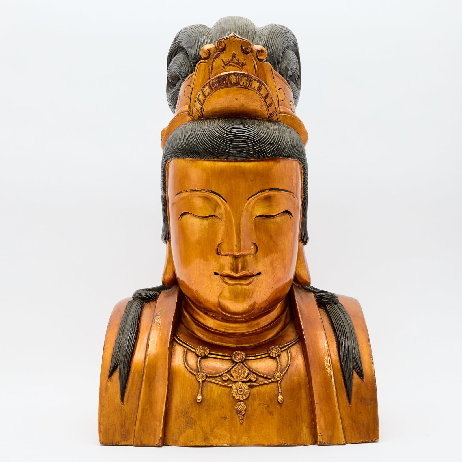 A Chinese Lacquered Wood Bust of Guanyin Late Qing Dynasty: Carved as Guanyin wearing a high chignon and jewelry, the rounded face flanked by a pair of long earlobes, with downcast eyes and a serene expression. (Height 20 1/2 inches)