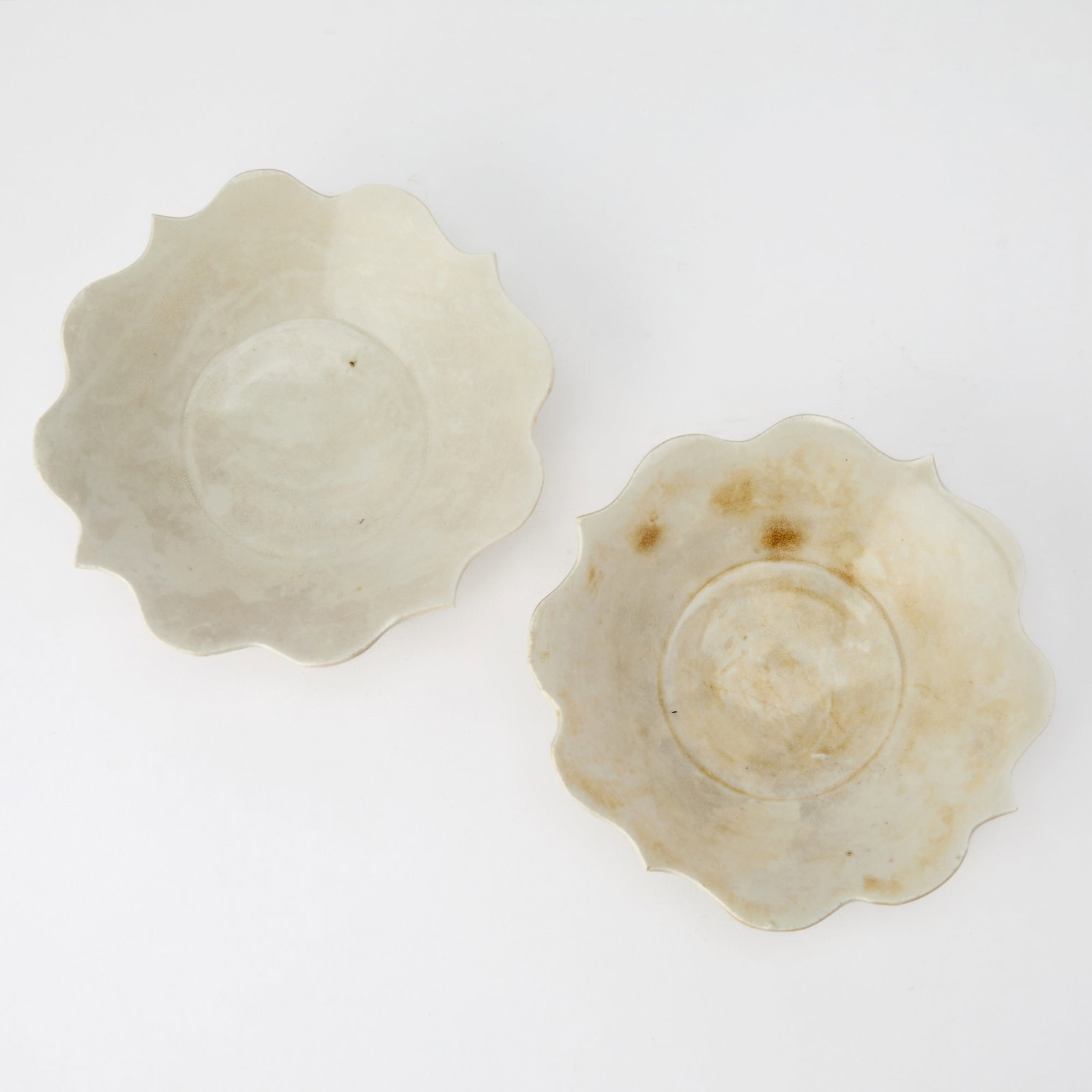 A Rare Pair of Chinese Quatrefoil Dingyao Bowls Five Dynasties-Early Northern Song Dynasty: The flaring sides rising from a thin foot ring and terminating in a bracketed, lotus-petal cut rim; the ivory toned glaze pooled in some areas and the base left unglazed to expose white porcelaneous b