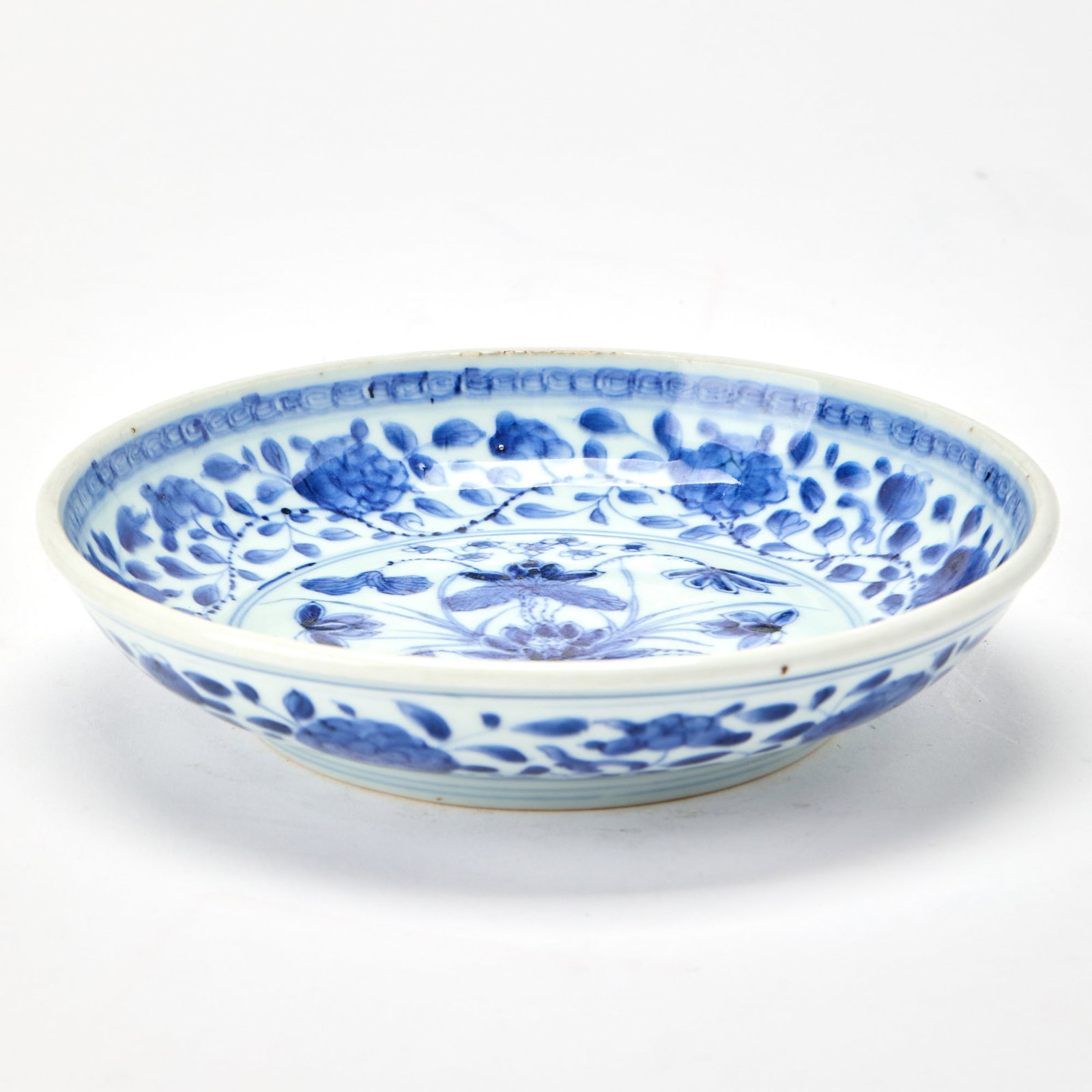 A Chinese Blue and White Porcelain ‘Lotus’ Dish Kangxi Period: Decorated with a lotus bouquet to the central circular medallion, surrounded by a wide border of scrolling leafy vines bearing blossoms. (Diameter 7 3/4 inches) Overall good condition.