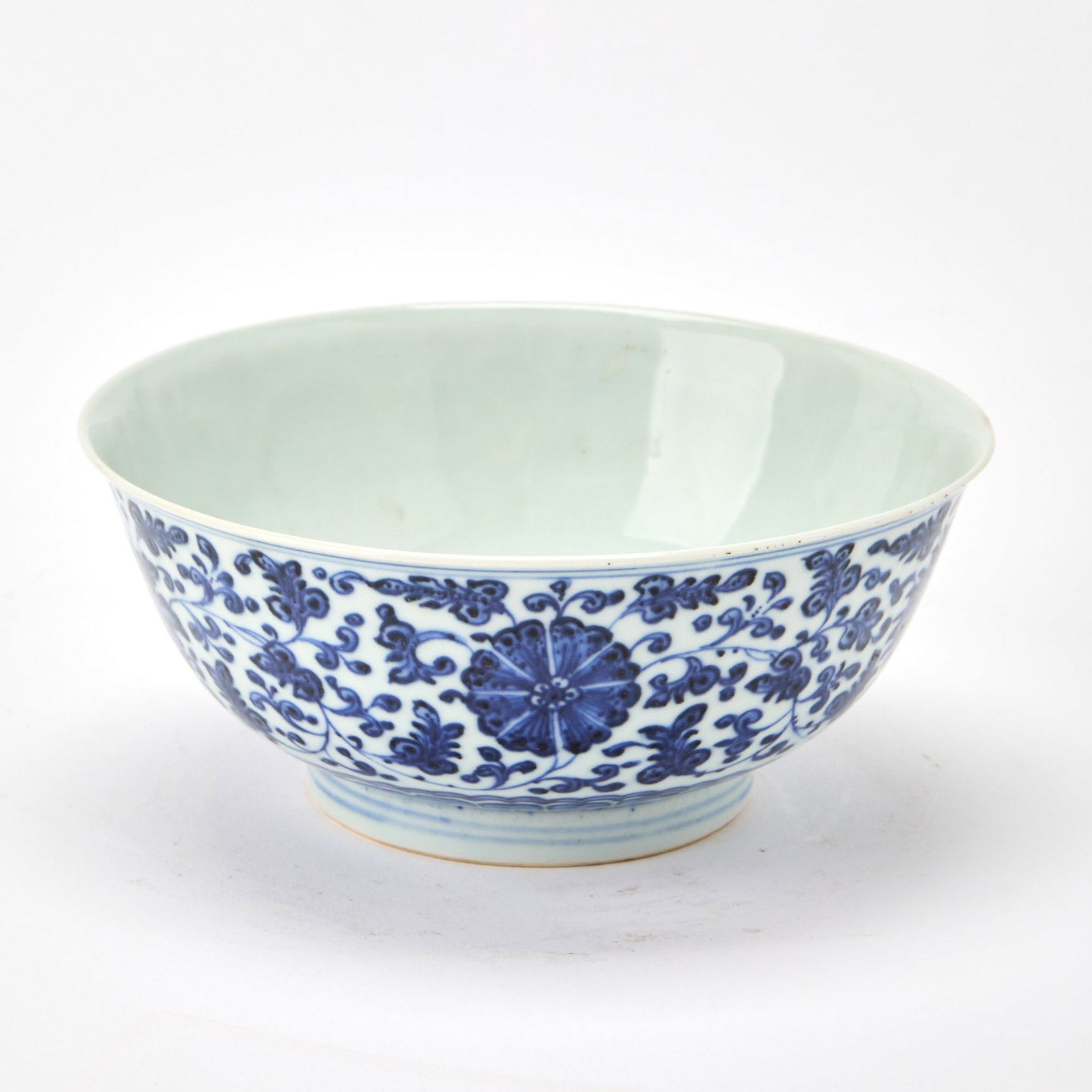 A Chinese Blue and White Porcelain Bowl Xuande Mark, Kangxi Period: With sides rising from a straight foot to a flaring rim, the exterior decorated with continuous scrolling leafy tendrils bearing blossoms. (Diameter 7 inches)