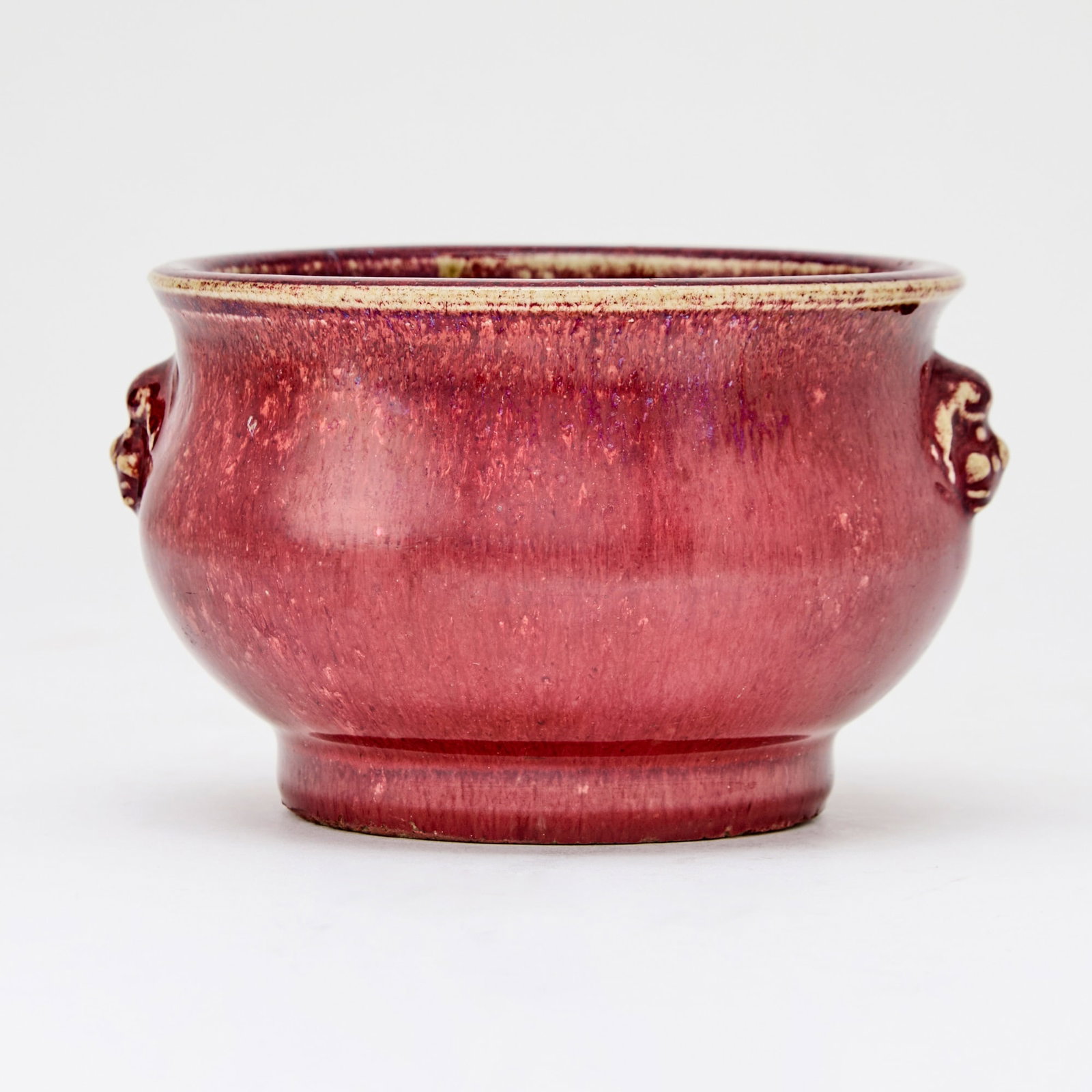 A Chinese Flambe Glazed Porcelain Censer 18th-19th Century: Of compressed form, applied with a pair of beast-form handles; covered in a crimson glaze streaked with lavender and mushroom tones. (Diameter 4 3/4 inches)
