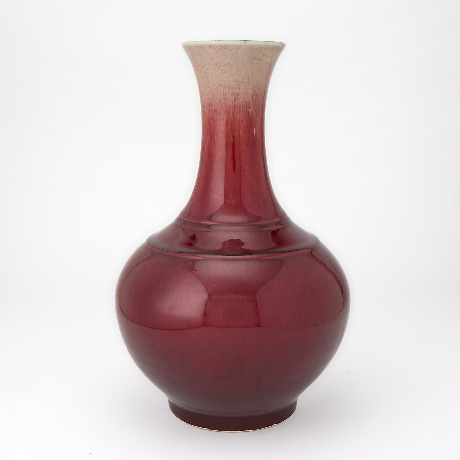 A Chinese Copper Red Glazed Porcelain Bottle Vase 19th Century: The ringed globular body surmounted by a trumpet neck, covered in lustrous oxblood red glaze thinning to rim. (Height 14 inches)