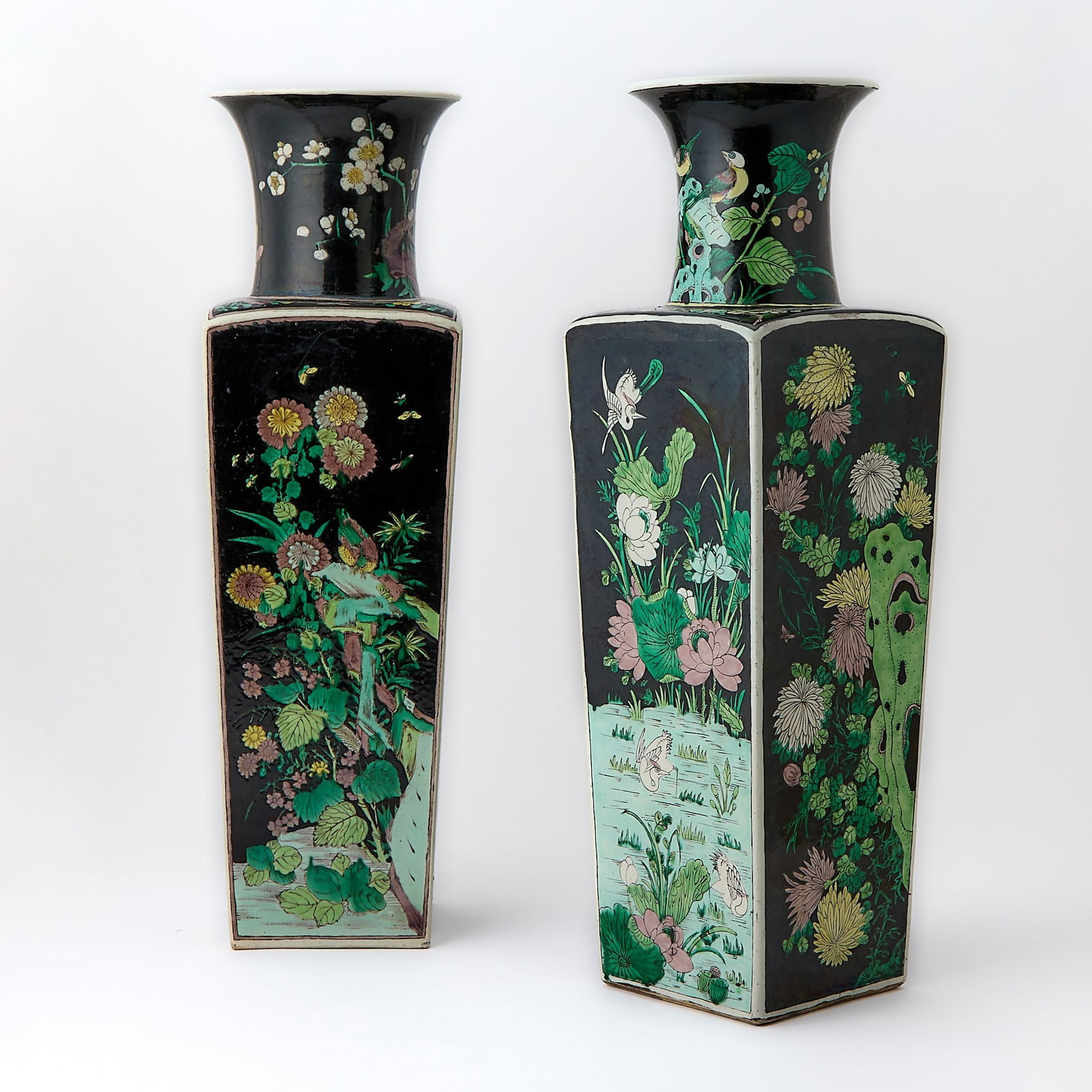 A Pair of Chinese Famille Noire Porcelain Square Vases Kangxi Mark, Qing Dynasty: Each has a square, tapering body surmounted by a concave neck, decorated with blossoming branches and stems emerging from grassy ponds or gnarled rocky outcrops, amidst which various birds and butterf