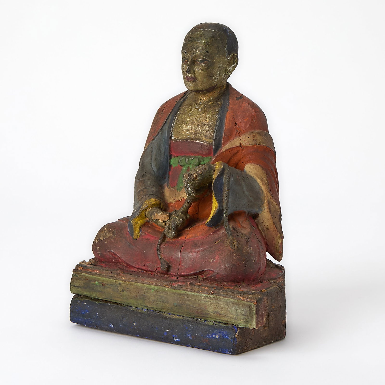 A Tibetan Polychrome Lacquered Wood Figure of a Monk 18th-19th century: Depicting the seated figure in vivid robes atop an austere, stepped base. (Height 8 3/4 inches)