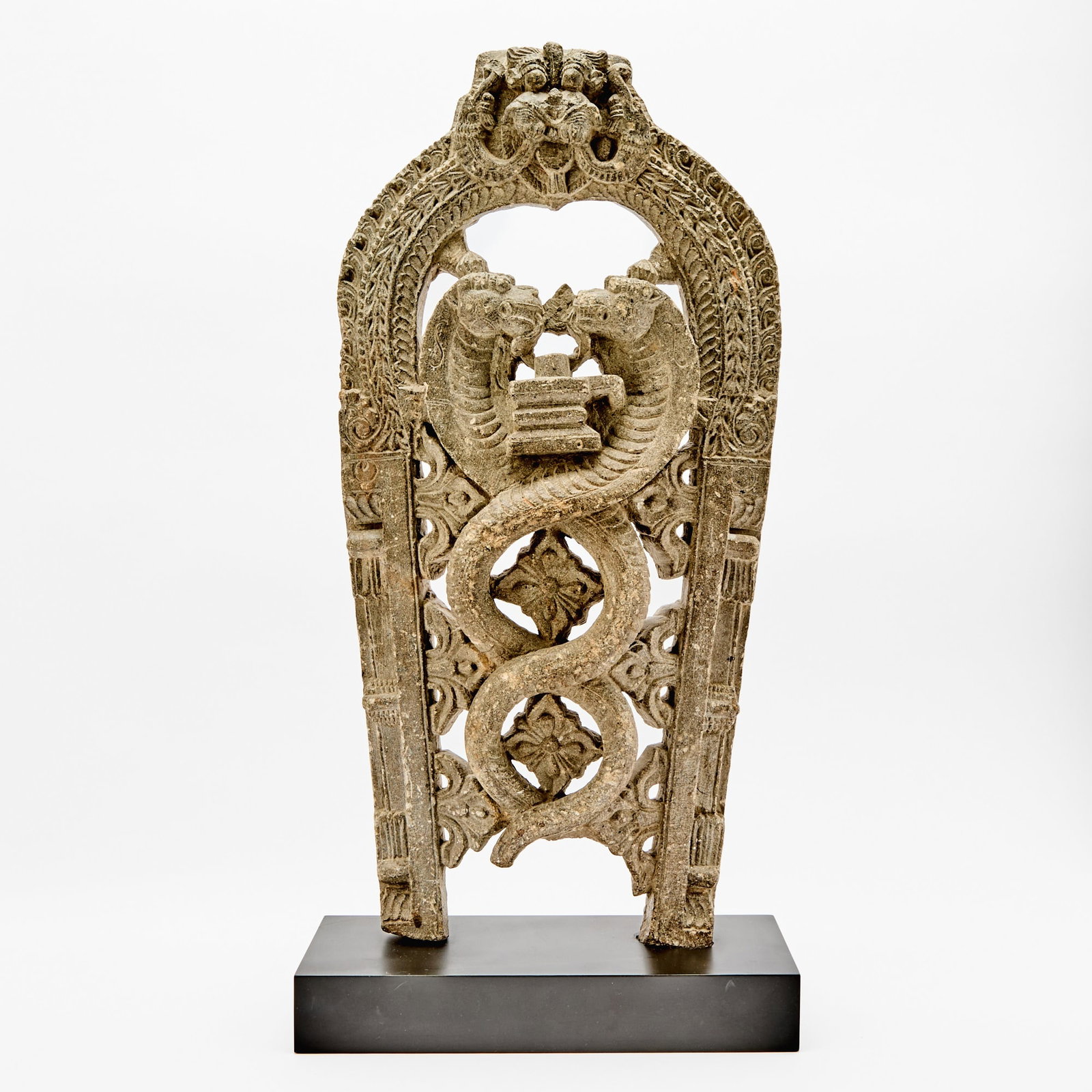 An Indian Carved Stone Stele of Siva with Cobras 17th-18th century: The openwork-carved arched stele tapering to base and showing two intertwined cobras with facing heads encircling the image of a lingam. (Height 24 1/4 inches)