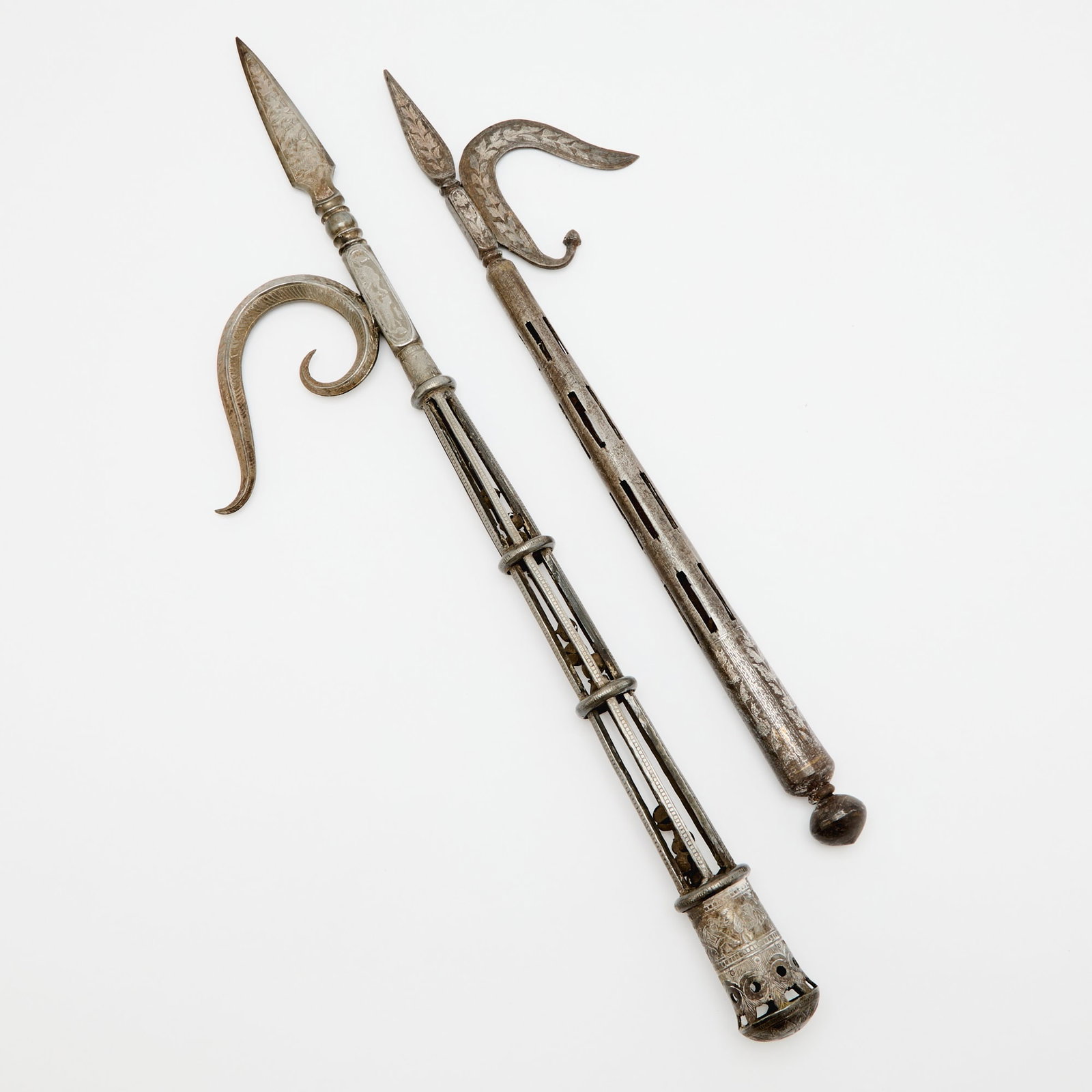 Two Indian Inlaid Steel Elephant Goads 19th Century: Of typical and similar forms, each handle cast with encased jingle bells and the handles, blades and pommels decorated in floral and zoological motifs. (Length of largest 25 inches)