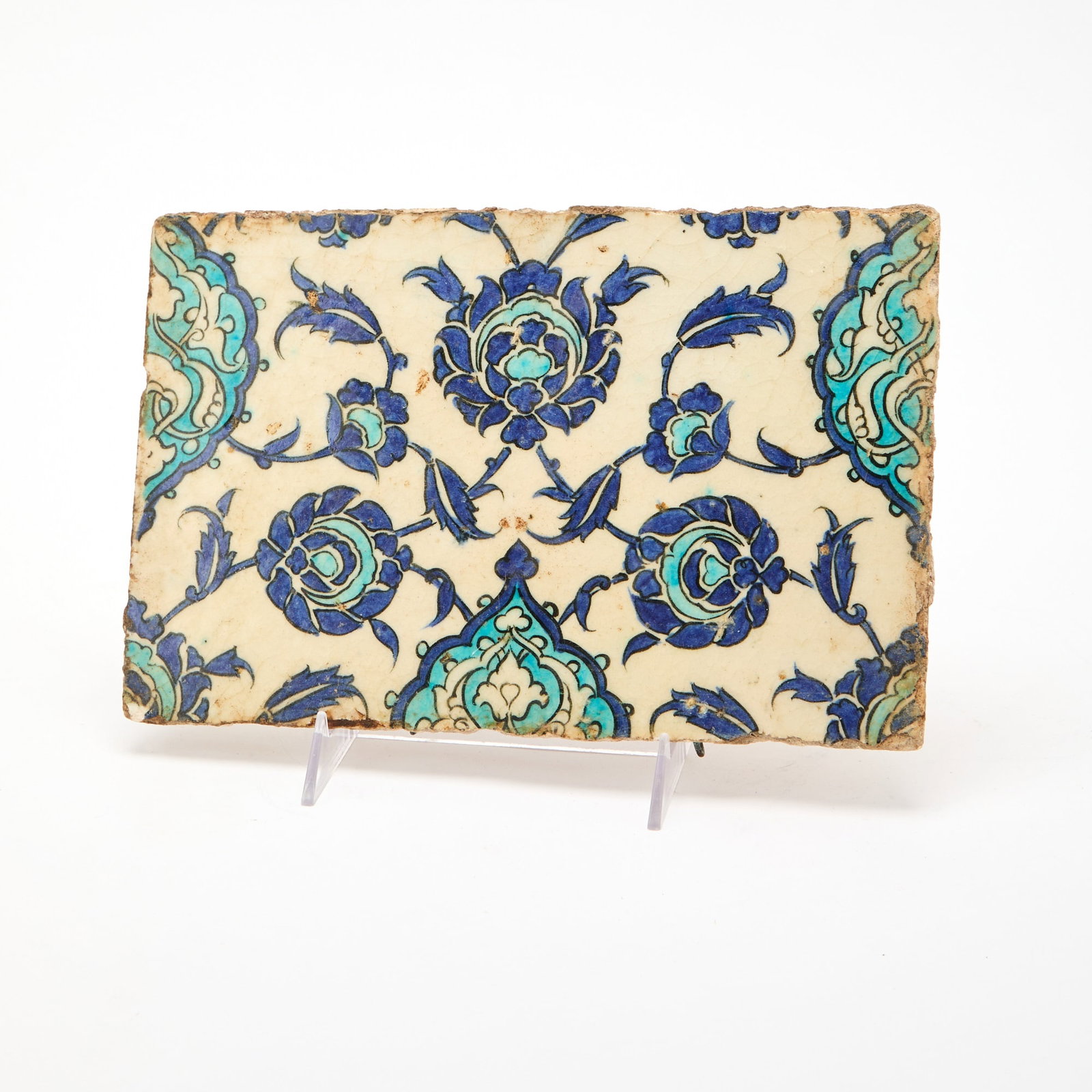 An Iznik Pottery Tile 16th Century: Decorated with a symmetrical design of interlocking leafy branches bearing blooms. (Length 11 1/2 inches)