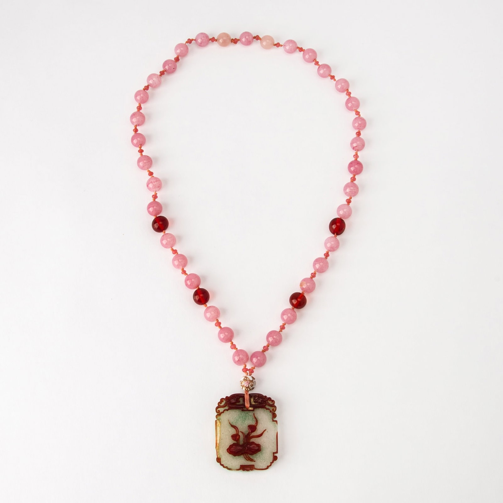 A Chinese Red and Green Overlay Glass Pendant 19th Century: Showing a red lotus over a snowflake white glass ground; strung with a pink glass beaded strand. (Height 2 inches)