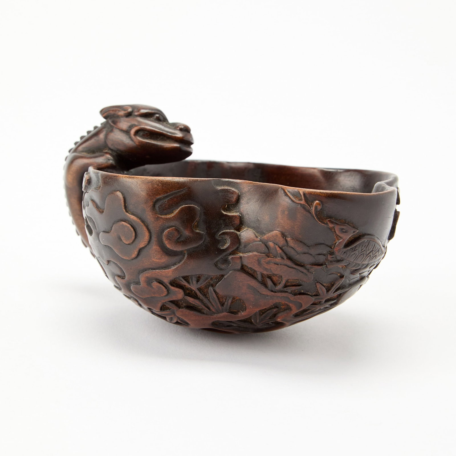 A Chinese Carved Boxwood Cup Qing Dynasty: The shaped, bowl-form cup carved with dragon handle and relief-carved clouds to exterior. (Length 5 inches)