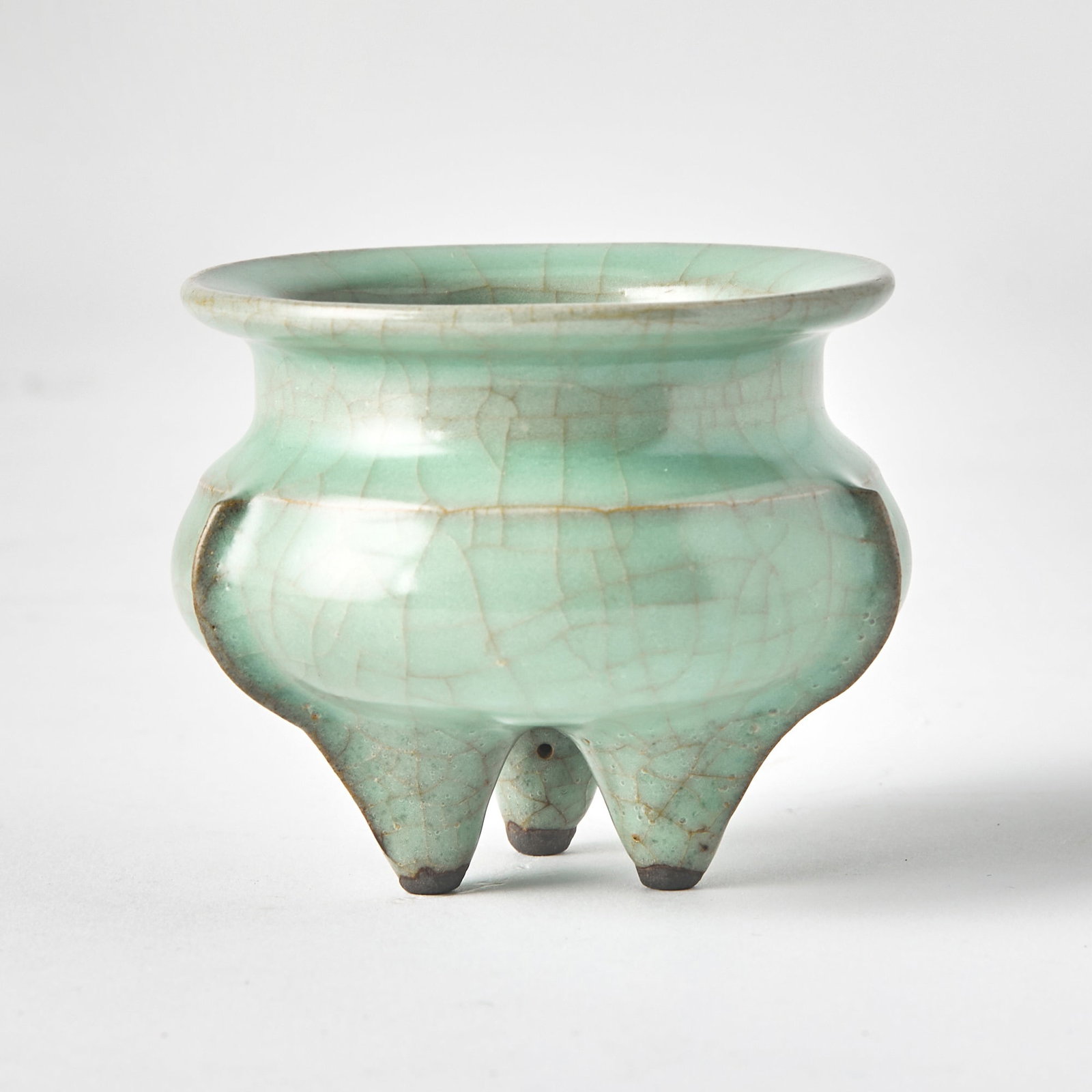 A Chinese Longquan Guan-Type Tripod Censer Ming Dynasty or Later: The globular body raised on three tapered feet and surmounted by everted rim with flat top; the sides with molded flanges extending to legs. (Height 2 3/4 inches)