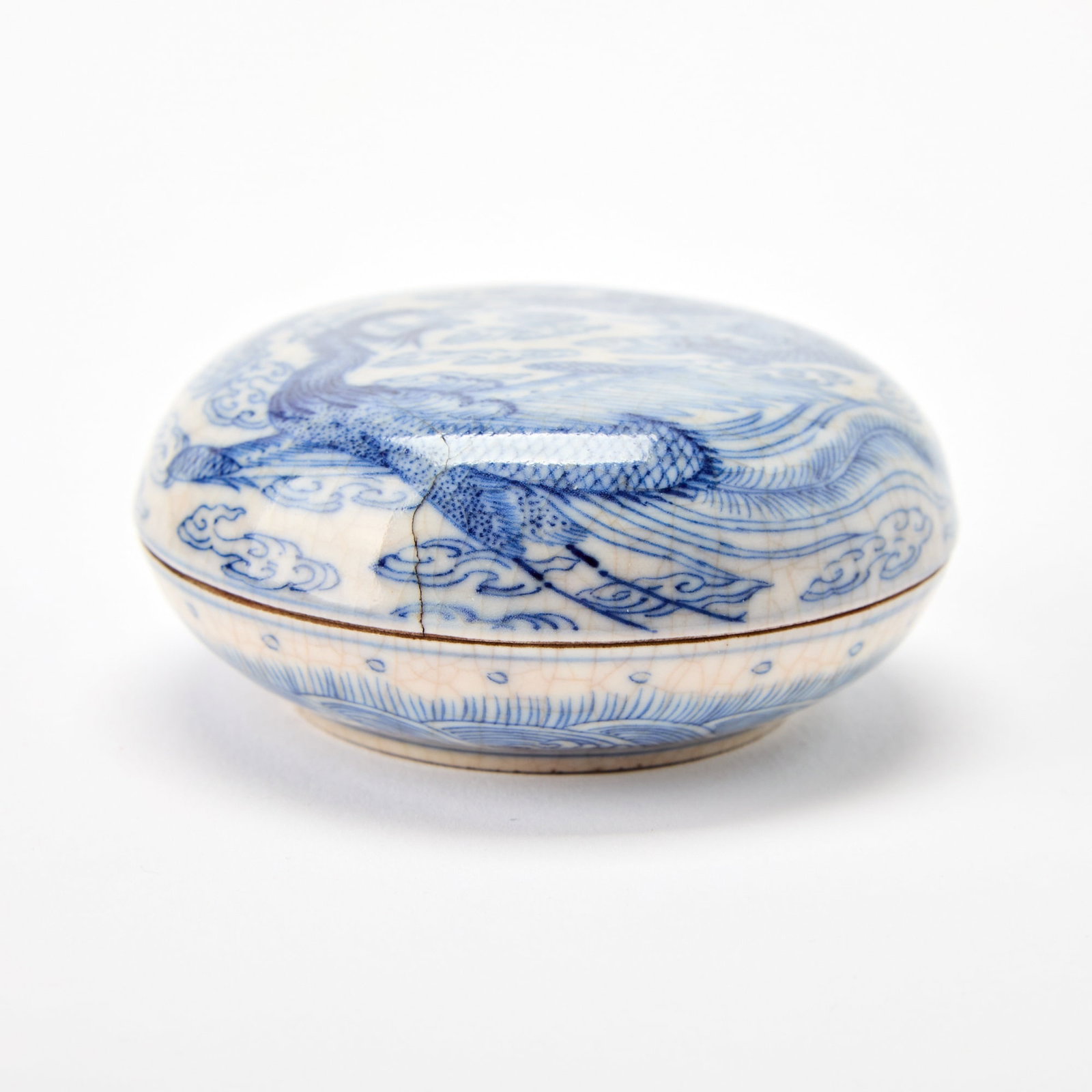 A Chinese Blue and White Porcelain Covered Paste Box Xuande Mark, 17th century: The domed cover adorned with a coiling dragon chasing a flaming pearl amidst cloud wisps; the sides with a wave band. (Diameter 3 1/2 inches)