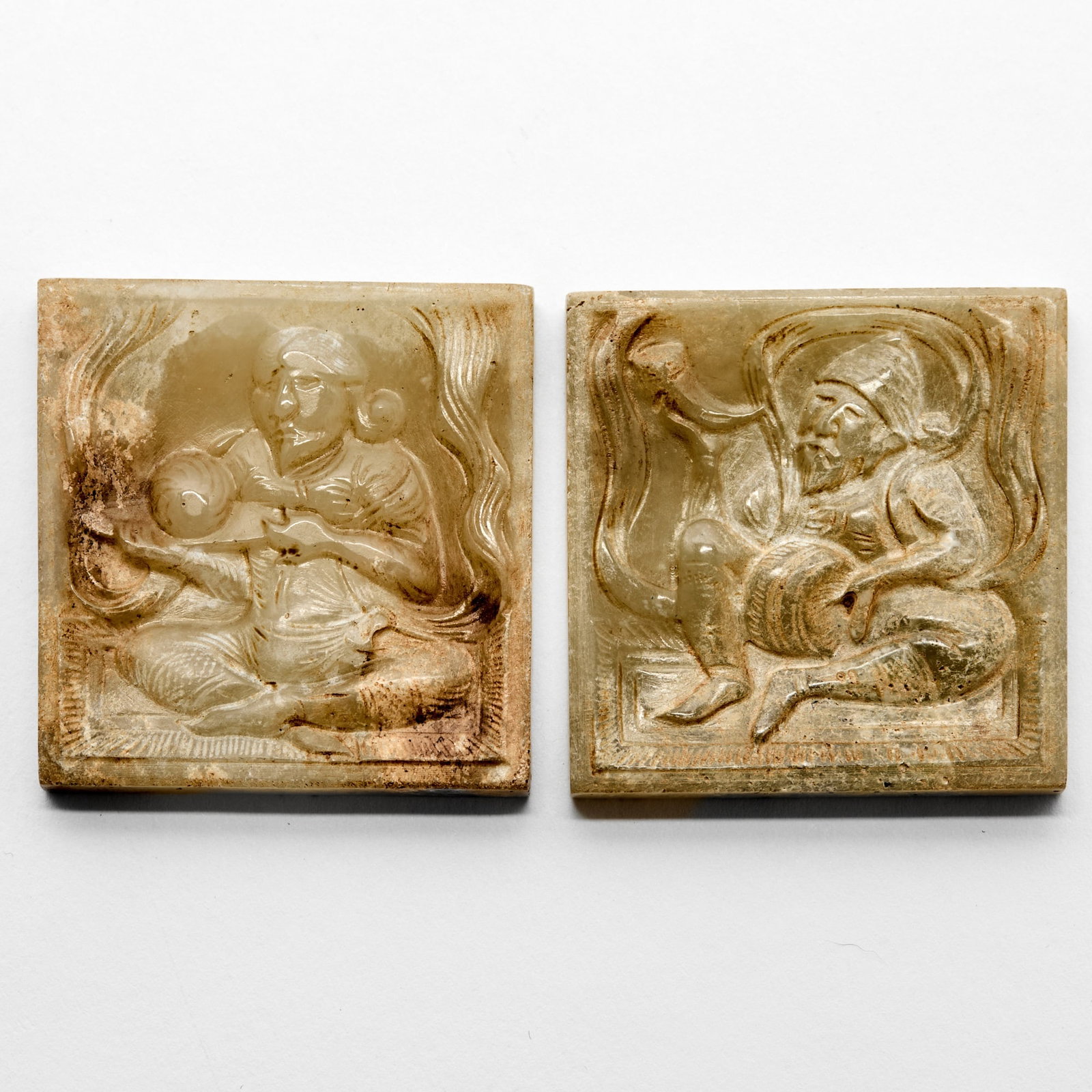 Two Chinese Jade Belt Plaques Tang Dynasty or later: Each of square form, carved a seated musician figure, the stone of celadon tone with russet coloring and inclusions. (Length 1 1/2 inches)