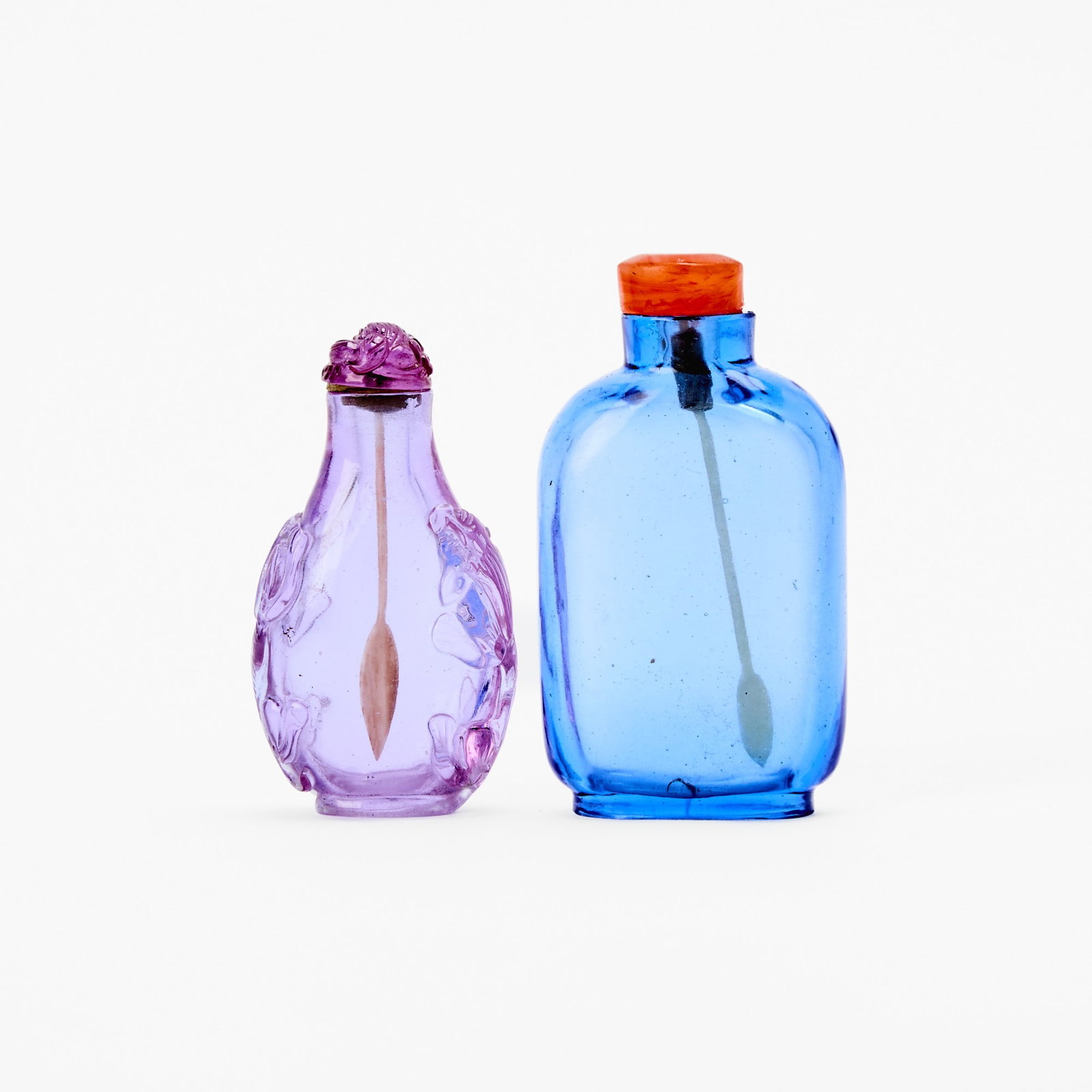 Two Chinese Glass Snuff Bottles 19th Century: Comprising a lavender-colored one carved with mythical beasts, and a blue, unadorned one. (Height of largest 2 1/2 inches)