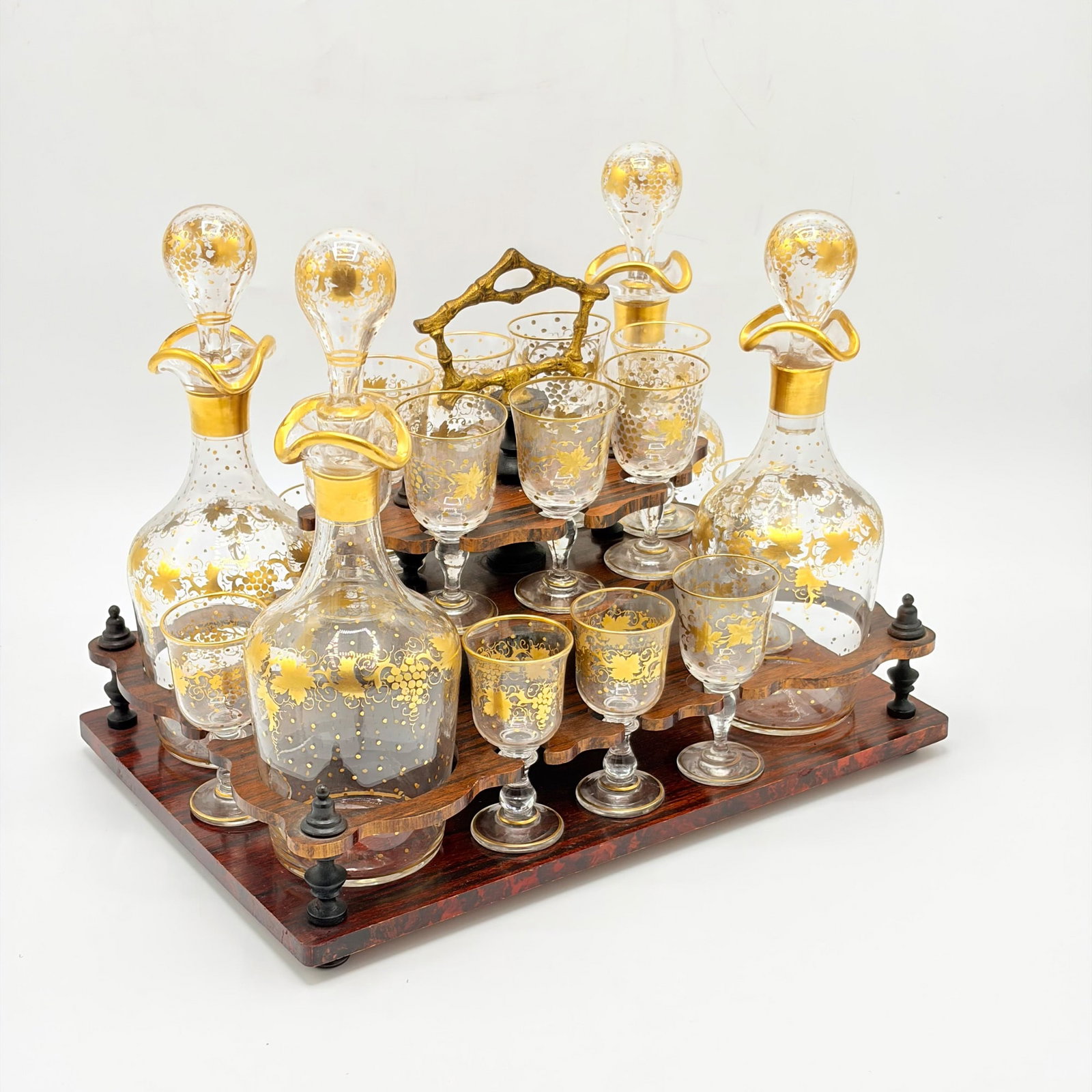 Gilt Glass Cordial Set: Late 19th century Comprising four stoppered decanters and sixteen glasses, in a fitted two-tier tray with gilt metal faux bamboo handle. Decanter height 9 inches.