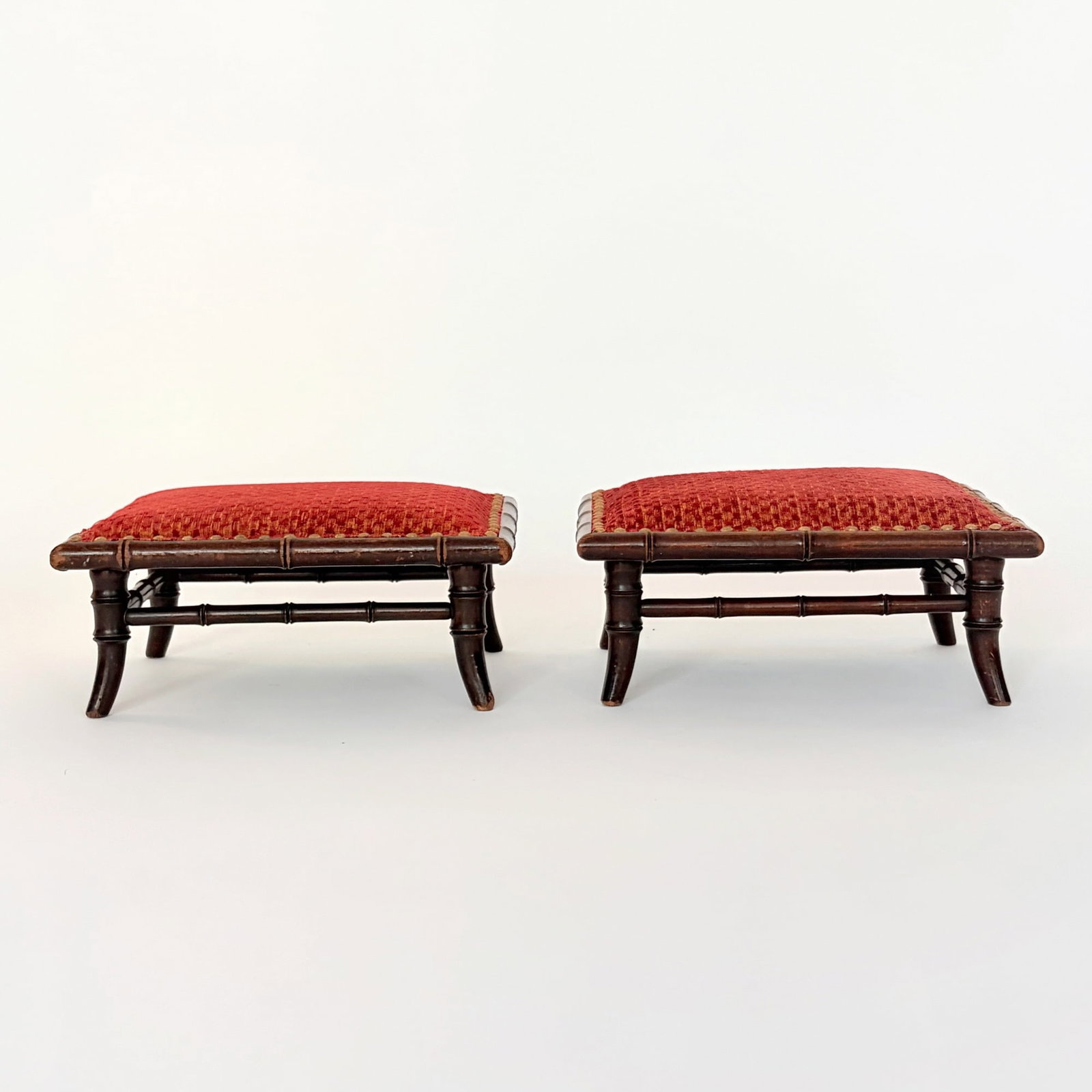 Pair of Faux Bamboo Footstools: Late 19th century The textured red upholstery lined with brass tacks, on flared feet. Height 6 inches, width 13 inches, depth 9 1/4 inches. edgewear