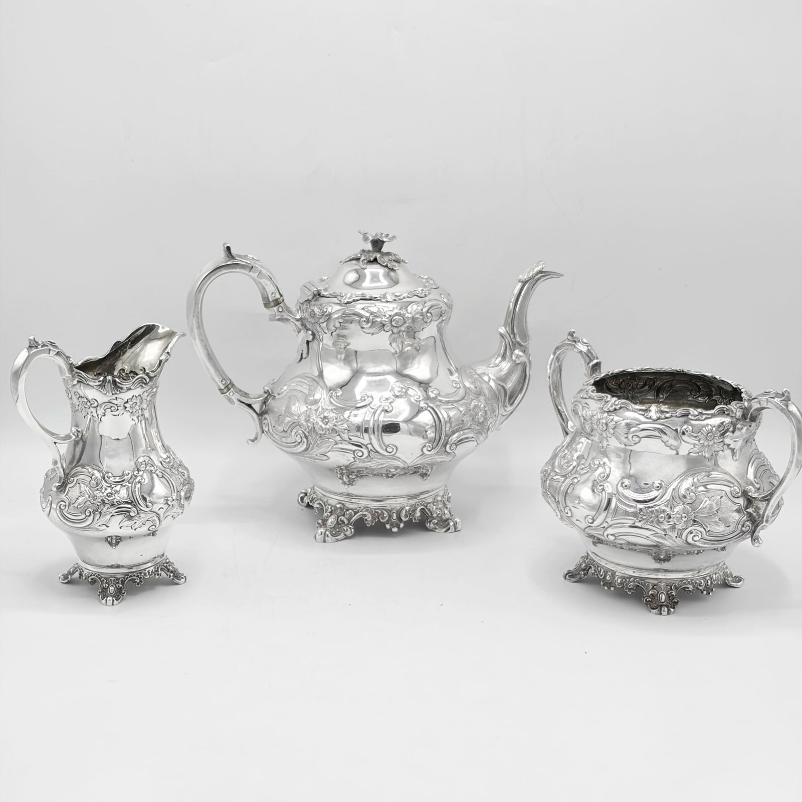 Victorian Sterling Silver Tea Service: John Wellby, London, 1847 Comprising a teapot, height 8 inches, open sugar, and cream jug, the baluster-form bodies chased with flowers and scrolls, on foliate bracket feet. Total approximately 52