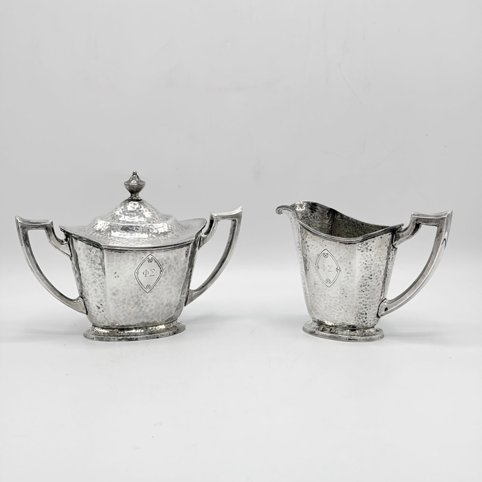 International Silver Co. Sterling Silver Cream and Sugar Set: Early 20th century Comprising a cream jug and a covered sugar bowl, each with angular loop handles and a hammered finish. Height of covered sugar 5 1/2 inches, total approximately 17 ounces.