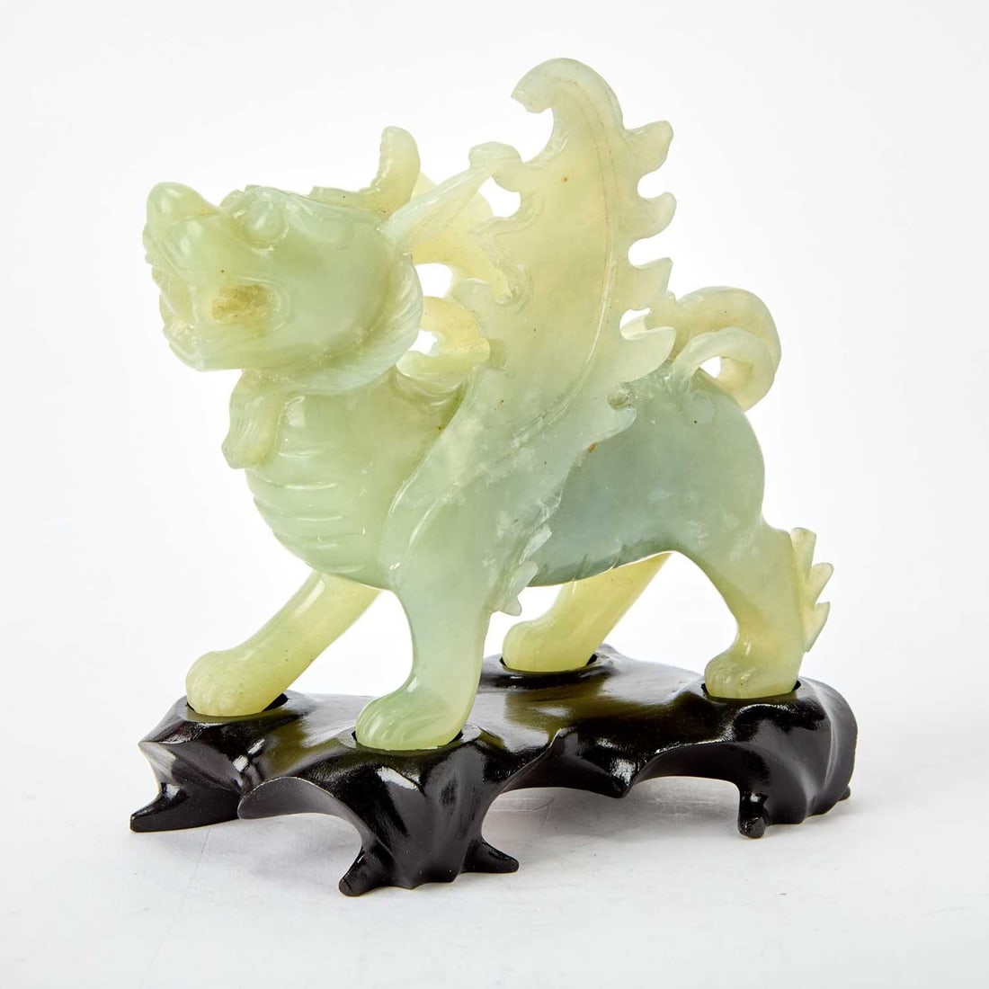 A Chinese Celadon Jade Carving of a Mythical Beast 20th Century: The winged figure standing foursquare, with bulging eyes and an open mouth. (Height 5 3/4 inches)