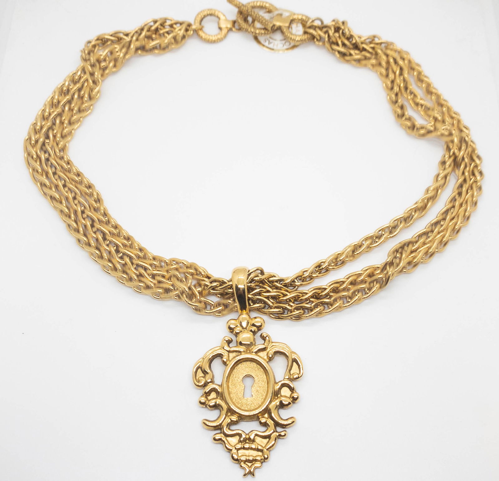 Vintage Rochas Gold Tone Triple Chain Link Necklace key: Vintage Rochas gold tone triple chain necklace with a toggle closure featuring a keyhole pendant. 20" long. Pendant 2" high x 1.5" wide. Marked on back Rochas. Still has original paper tag.