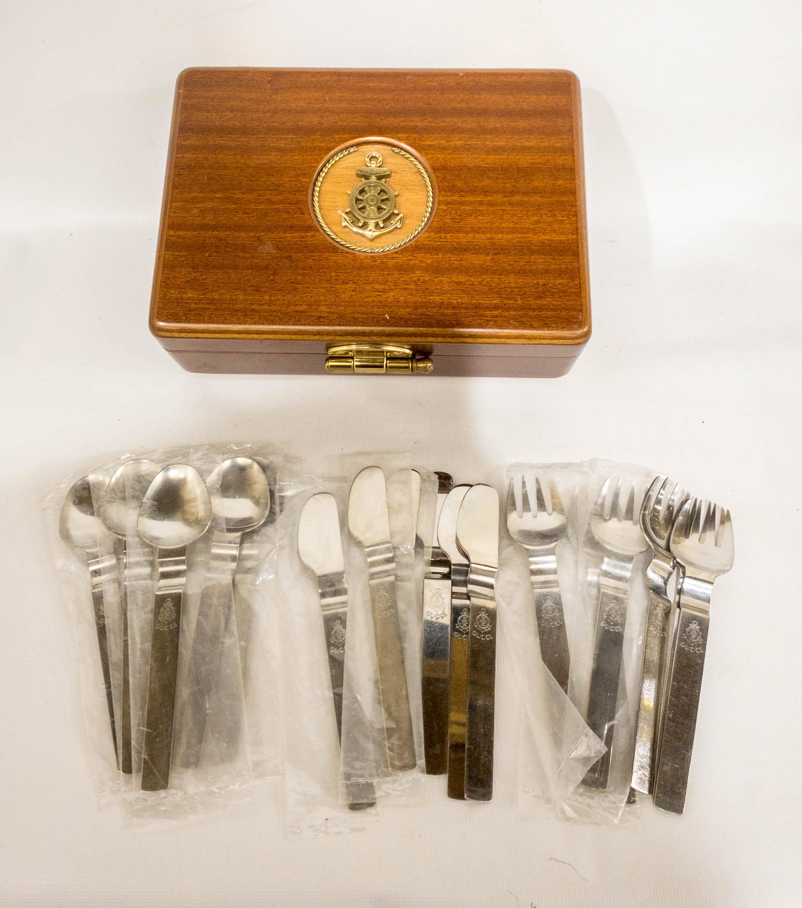 Rare 1980's Gucci Nautical Stainless Silverware Set in: A rare Gucci set of stainless silverware including 6 forks, 6 spoons, and 6 knives with a nautical wheel, anchor, and Gucci on each piece. They are in a luxurious wood box with brass hardware and the 