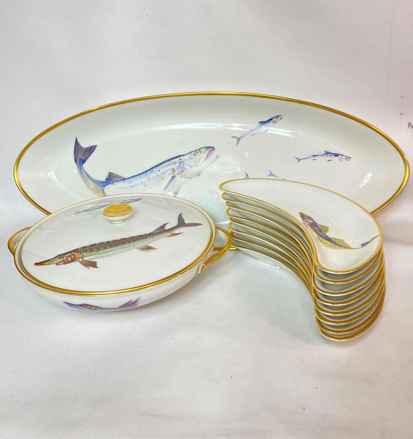 H & Co Selb Bavaria Germany Heinrich Fish Set Porcelain: H & Co Selb Bavaria Germany Heinrich fish set including a large platter, 23" long x 8.75" wide, a lidded tureen 3" high, 9" diameter, and 8 curved plates, 9" long x 3.5" wide. All marked on bottom.