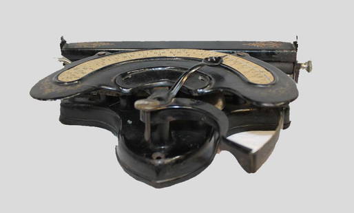 Early Typewriter: Early typewriter in black enamel paint finish with gold designs on top corners. Unit works by selecting different characters with a pointer, then depressing lever. Approximately 10 x 6 x 3" high.