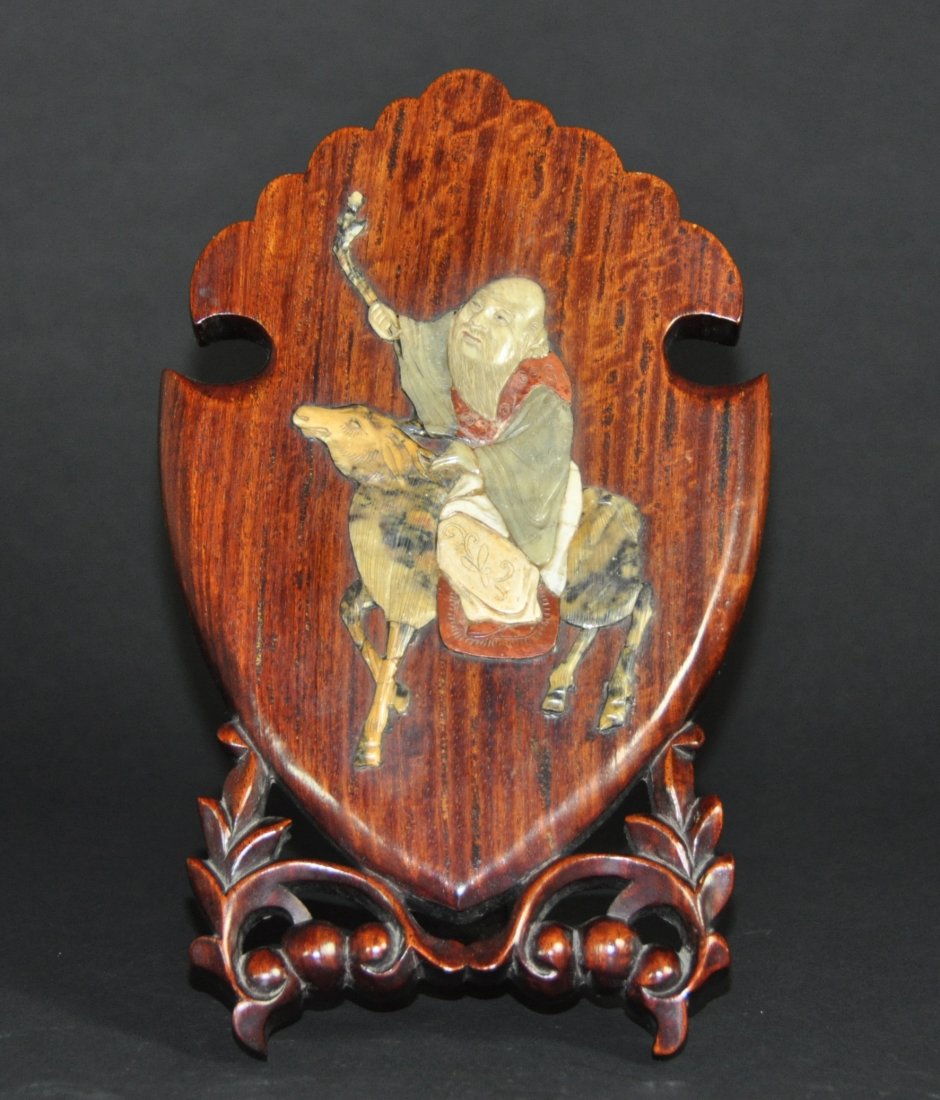 A Qing dynasty Huanghuali wooden plaque: This piece depicts a sagely wige atop of a deer-like animal. Both depictions are made from Shoushan stone and the surrounding wood is Huanghuali. Height 27 cm, Length 16.5 cm