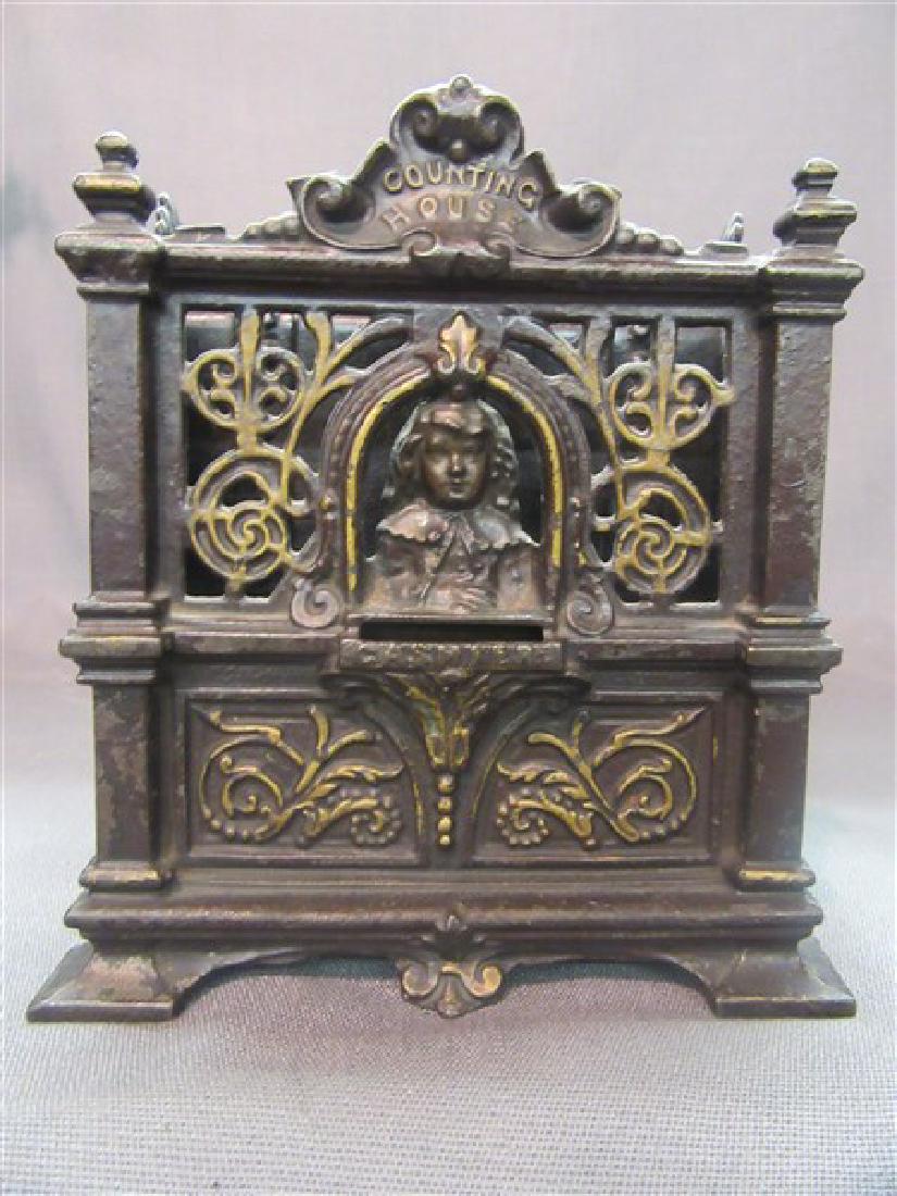 Barton Smith Cast Iron Fidelity Trust Still Bank: Counting House "Fidelity Trust Vault" Still Bank. This large bank measures 6" wide by 5-1/2" deep by 6-1/2" high. Made from cast iron. Even patina overall finish with gold highlights. Features lady ca