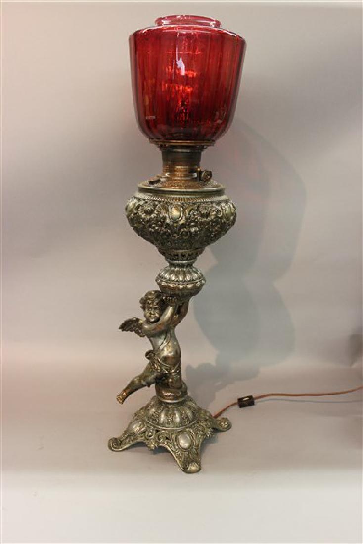 Victorian Silver Plated Cherub Lamp: A Victorian silver plated cherub lamp with cranberry glass shade. Dimensions: 29"h X 9"d