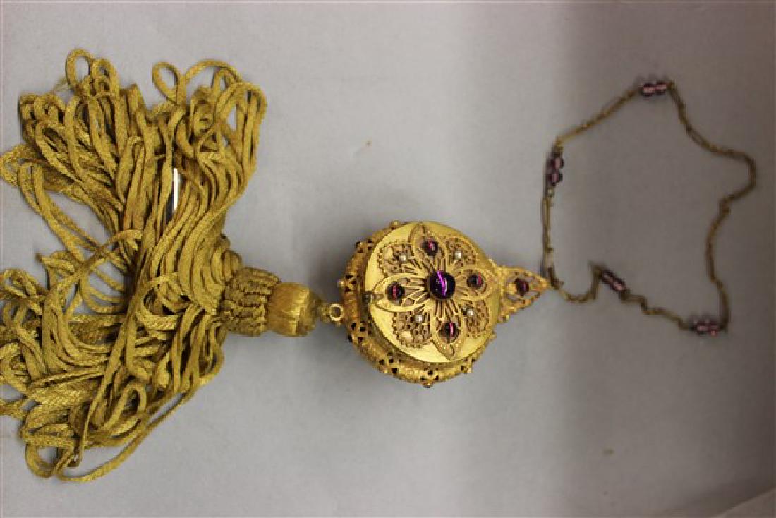 Trinity Plate Vintage Jeweled Compact Necklace: A fine and unusual compact necklace with glass amethyst cabochon style insets and faux seed pearls. Fine filigree work. Tassel at bottom has concealed lipstick holder. Dimensions: 16 1/2" length and c