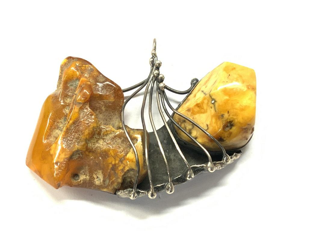 Large Brutalist Amber And Sterling Silver Pendant: A large Brutalist style chunk of a amber with bold sterling silver frame holding in position. A nice necklace pendant,initialed illegibly and marked 925 on bail. c.1970's or 80's. Dimensions: 3 1/4"w 