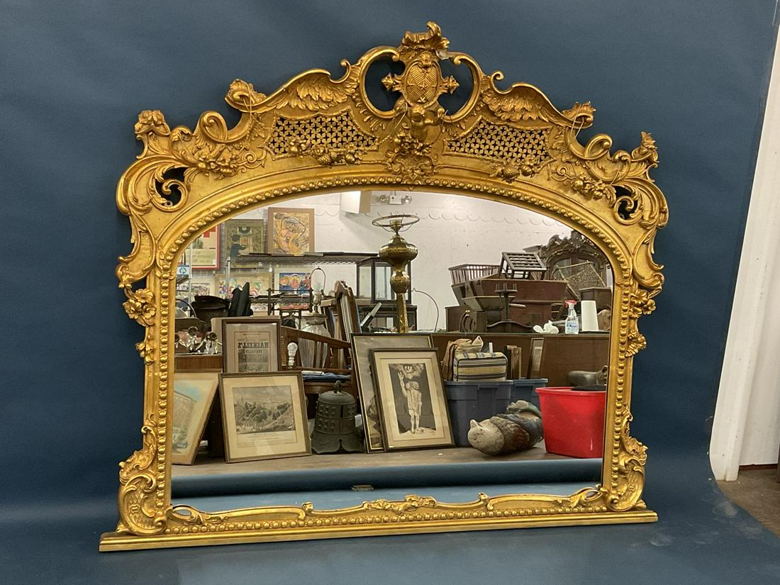 American Carved Gilt Wood Baroque Style Mirror: American carved gilt wood frame and gesso arched overmantel mirror, Baroque pierced crest with putti and fruit garland. Matching cornice lot number 170. Dimensions: 75 7/8” x 66 1/8”.