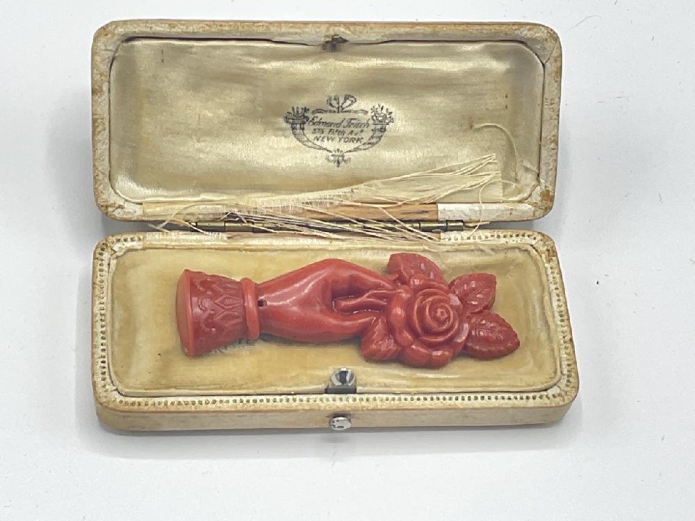 Early Carved Bakelite Hand Holding Flowers Pin: Early carved Bakelite articulated hand holding flowers pin. Coral color. Appearing to be housed in original box. Dimensions: 2 1/4" X 3/4"