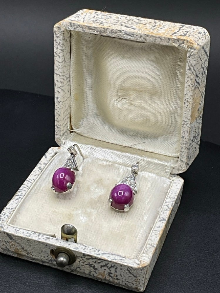 14K White Gold Synthetic Star Ruby and Diamond Earrings: 14K White Gold Synthetic Star Ruby and Diamond Earrings.Two synthetic oval star ruby stones and eight (8) single cut diamonds. Earrings have hinged leaver backs. Total weight: 3.7 grams.