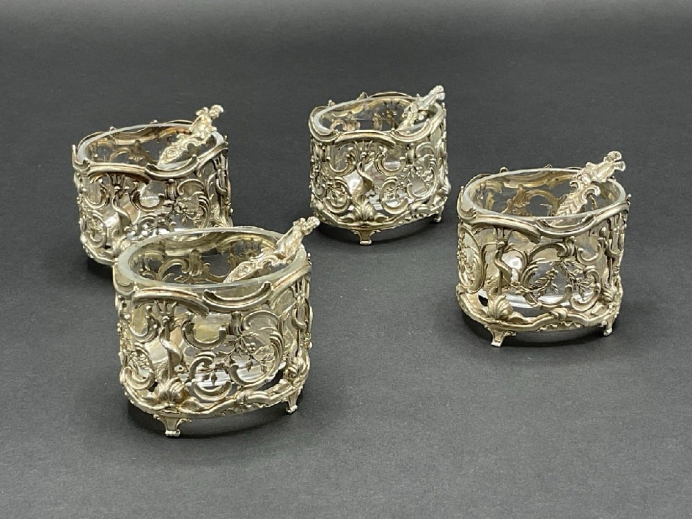 Four (4) Sterling Silver Salts and Spoons: A set of four (4) sterling silver sea-life themed openwork sterling silver salts with glass inserts. Four (4) sterling silver salt spoons with figural cherubs. Dimensions: 1 1/2” x 2” Tota