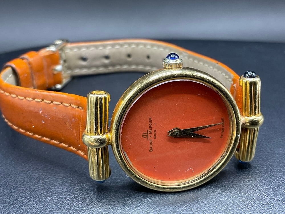 18K Yellow Gold Baume and Mercier Lady's Wrist Watch: 18K Yellow Gold Baume and Mercier Lady's Wrist Watch. Having cabochon blue spinel stone accents. One stone is missing. Please see photograph preview. Dimensions: 1 1/4” dial