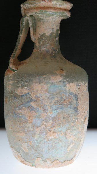 Ancient Roman Art Glass Handled Bottle: An Ancient Roman art glass single handled bottle. Appearing all intact. Very thin. Green iridescent color. Dimensions: 5" height X 2.5" width.