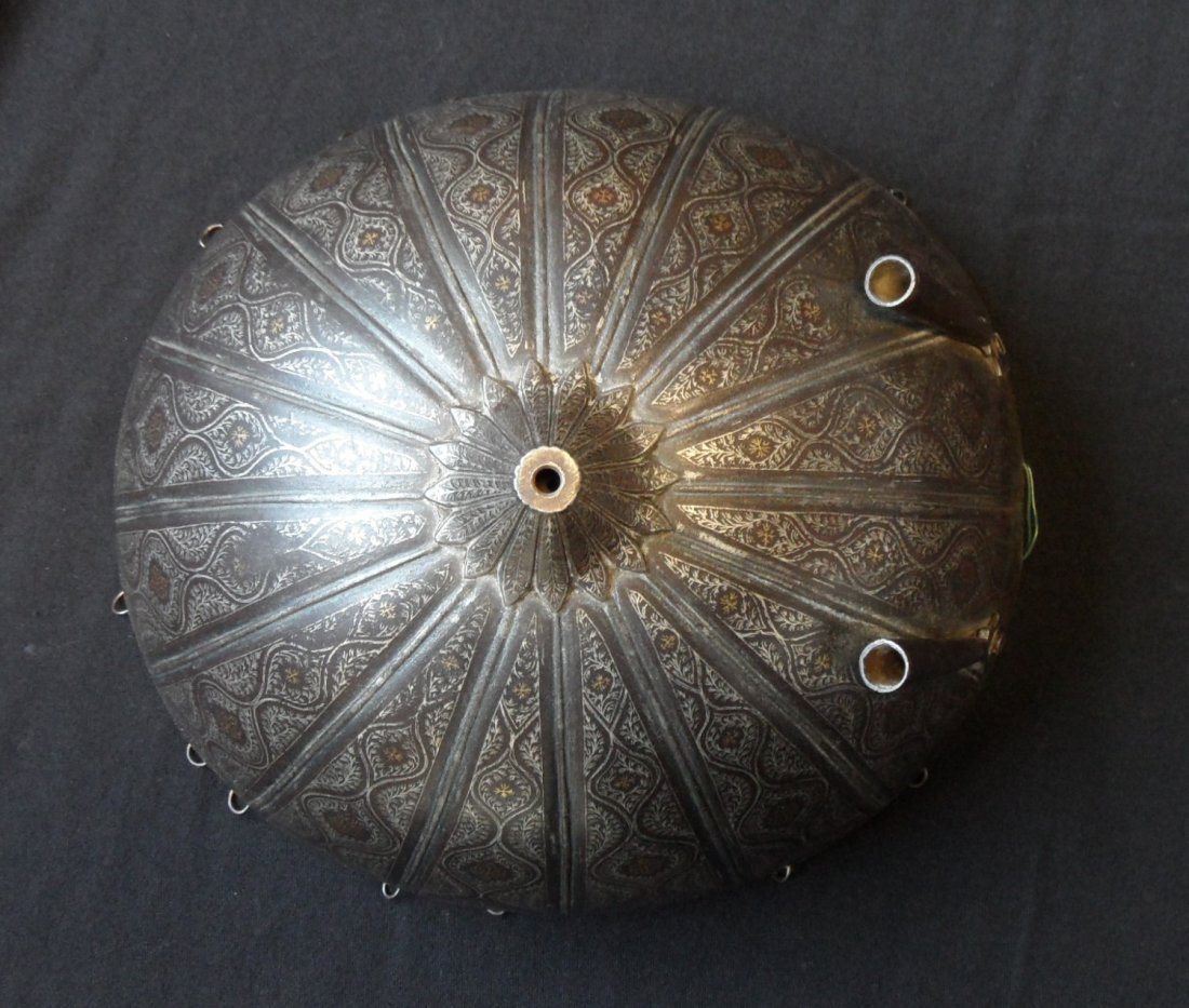 **AN INDO-PERSIAN HELMET (KULAH KHUD), 19TH CENTURY: **AN INDO-PERSIAN HELMET (KULAH KHUD), 19TH CENTURY with hemispherical skull embossed with a radiating pattern of ribs rising to a foliate moulding for a central spike (now missing), fitted with a pai
