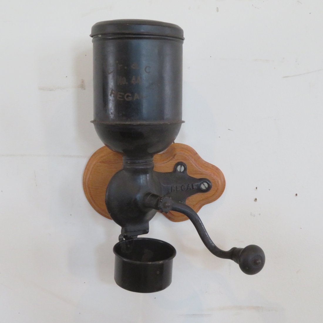 Regal tin and iron wall mount coffee mill: Regal tin and iron wall mount coffee mill, no. 44, mounted on oak contemporary board and has a tin cup, original stenciling, 13" x 5" x 5"